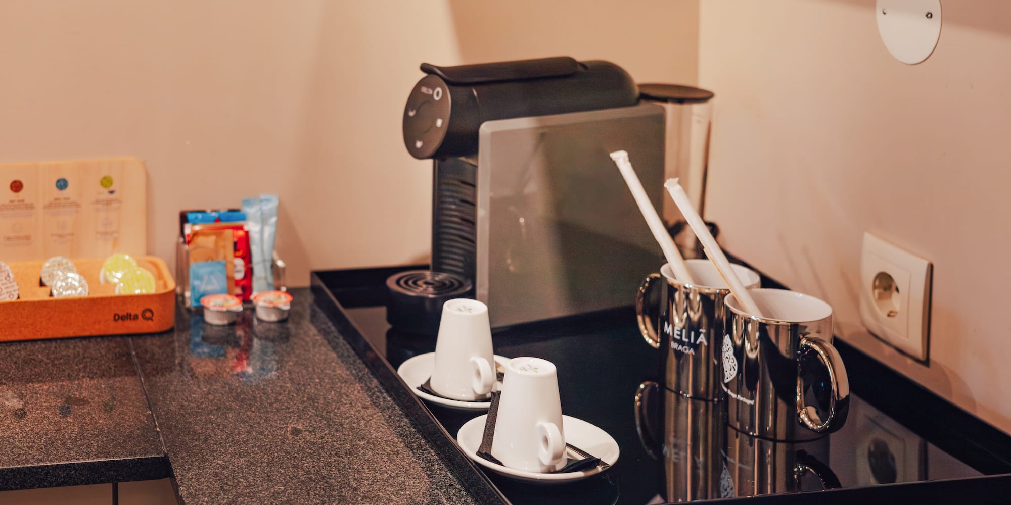 Hotel coffee station with espresso machine, Delta Q pods, white cups, and Melia Braga mugs.