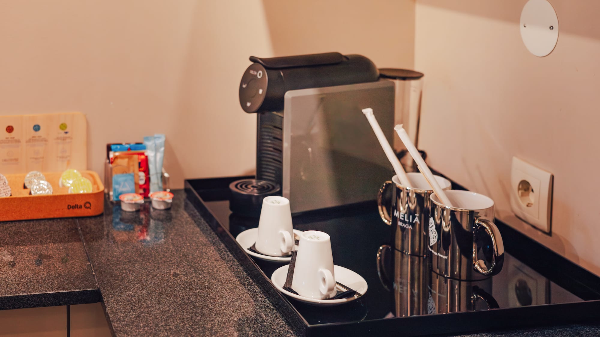 Hotel coffee station with espresso machine, Delta Q pods, white cups, and Melia Braga mugs.