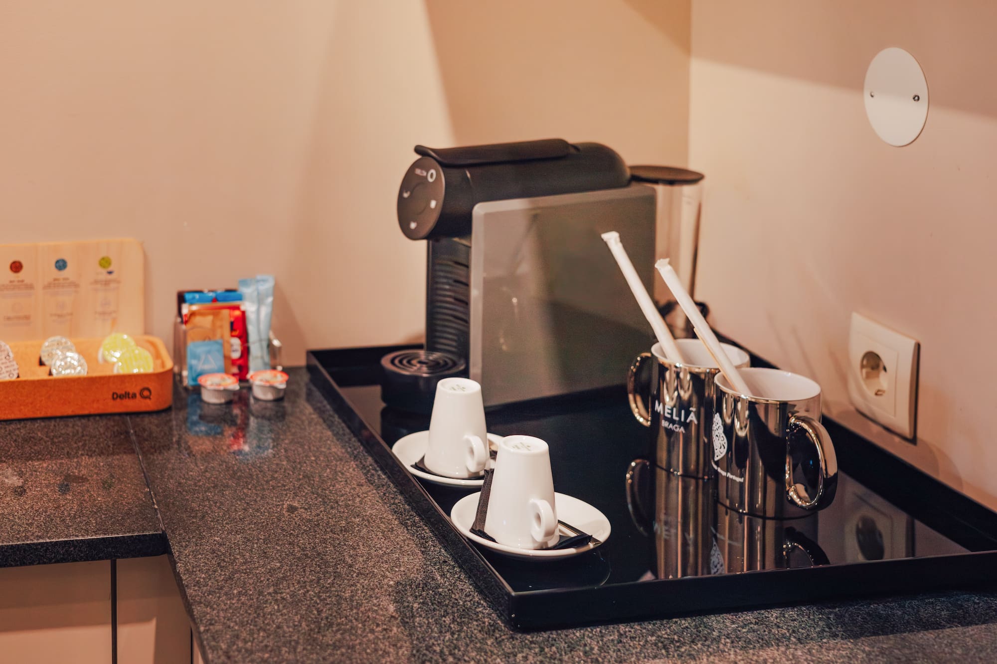 Hotel coffee station with espresso machine, Delta Q pods, white cups, and Melia Braga mugs.