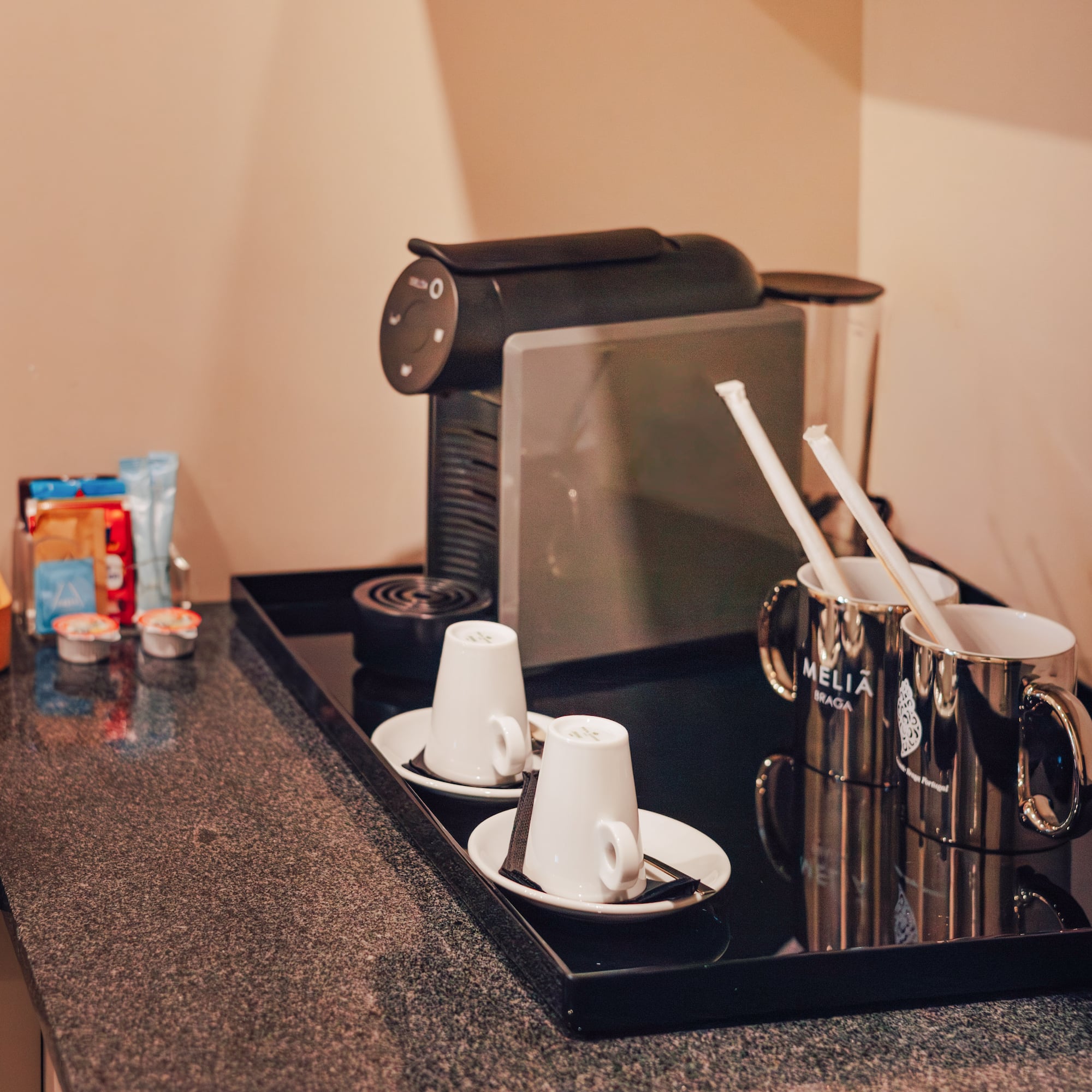 Hotel coffee station with espresso machine, Delta Q pods, white cups, and Melia Braga mugs.