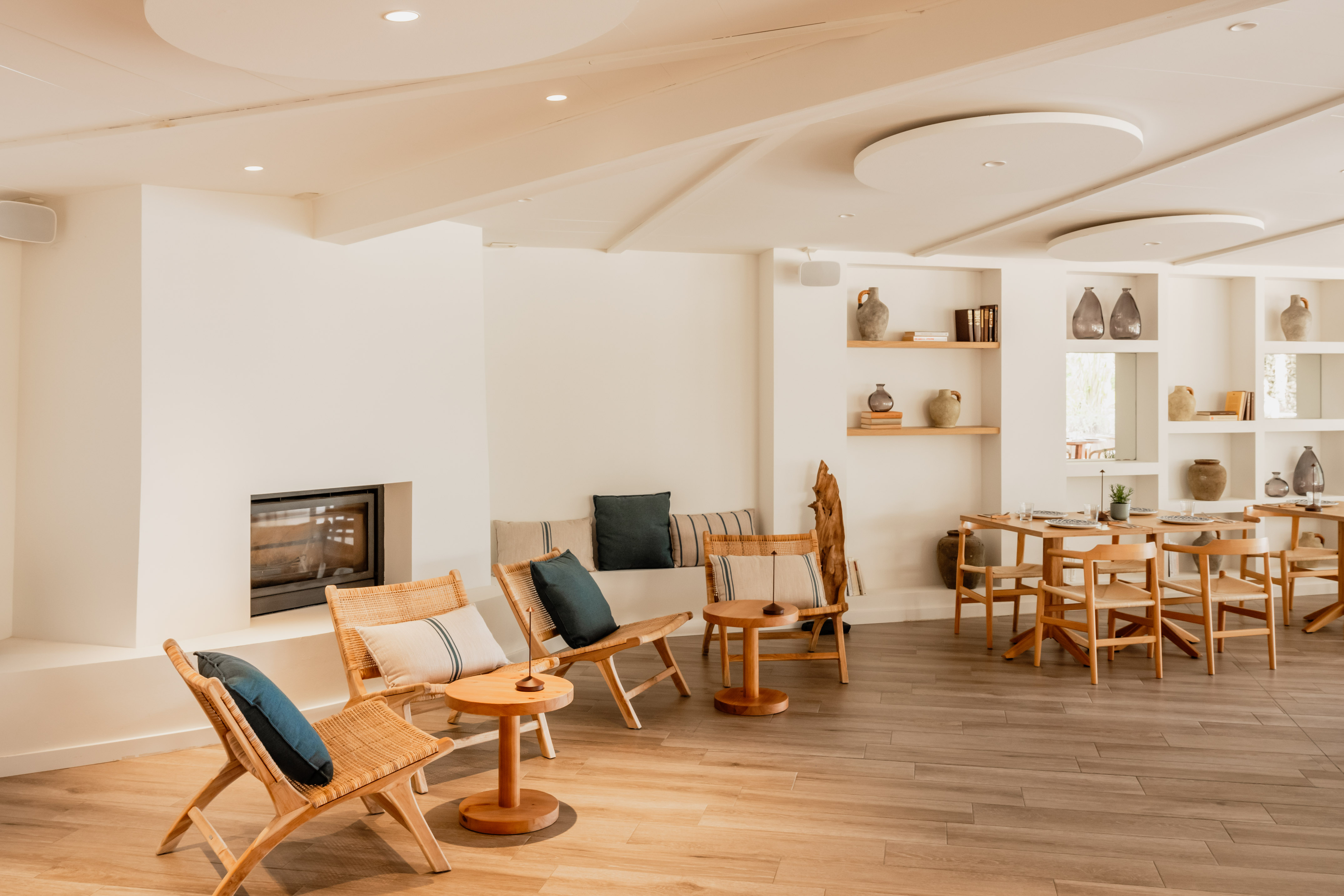 Modern lounge and dining room with wood furniture, fireplace, and minimalist decor.
