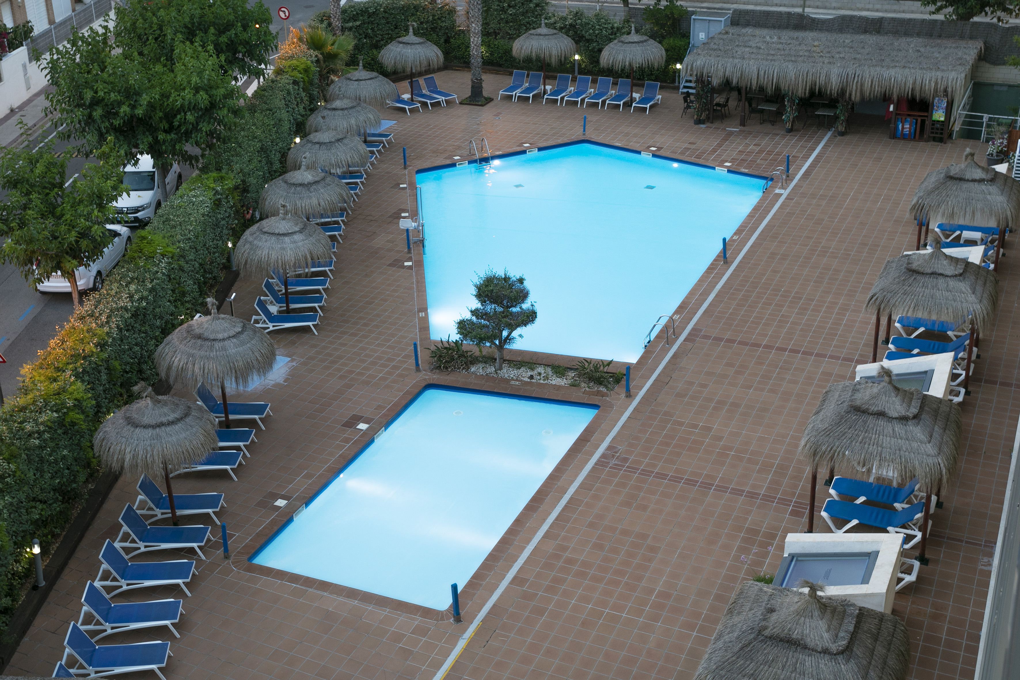 Resort swimming pools with blue loungers, terracotta tiles, and thatched parasols.