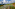 Green rice terraces with water reflecting sun, distant mountains, blue sky.