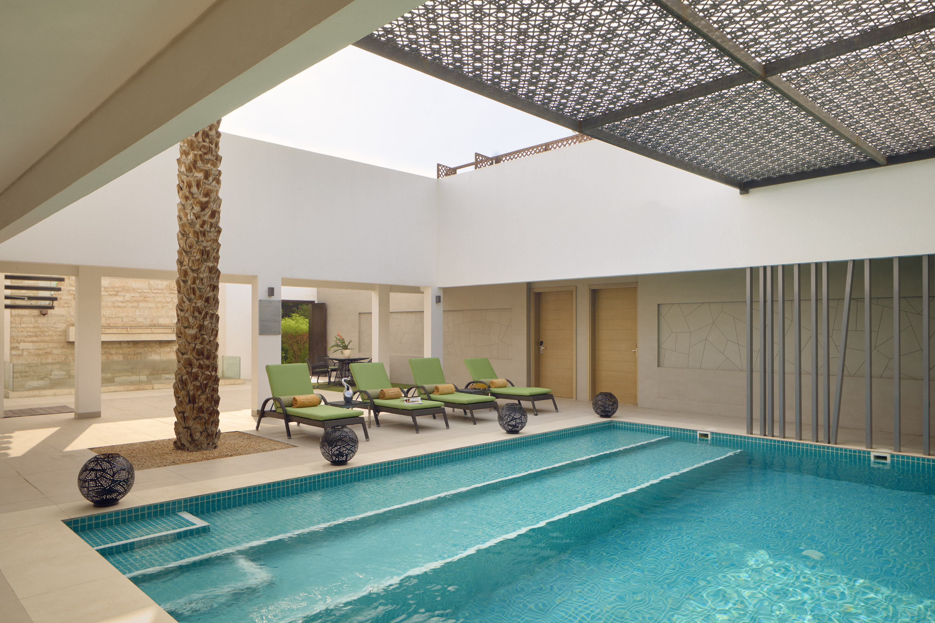 Modern resort pool with green loungers, palm tree, and patterned overhead pergola.