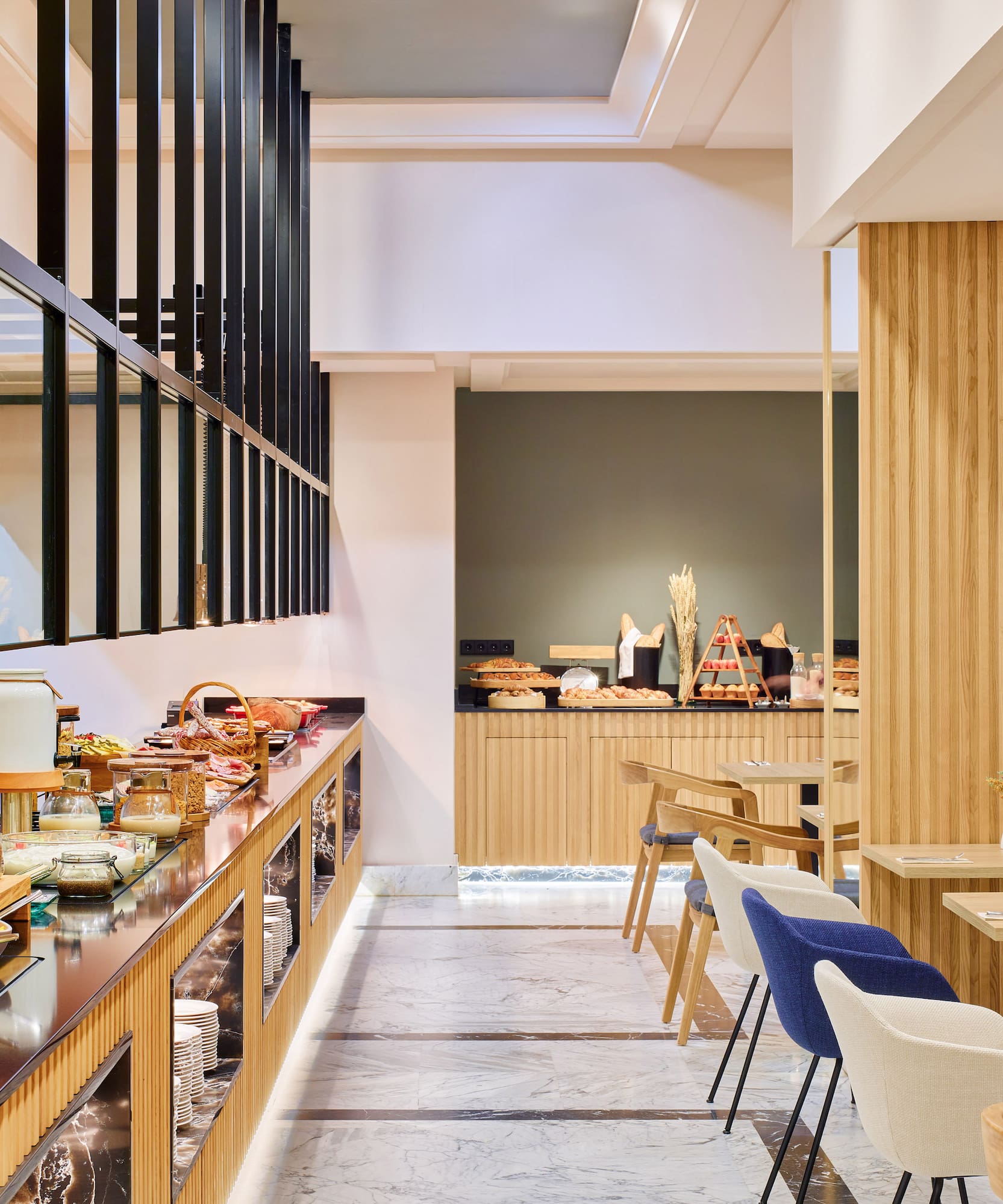 Buffet de desayuno moderno en hotel, con frutas, cereales y zona de mesas.