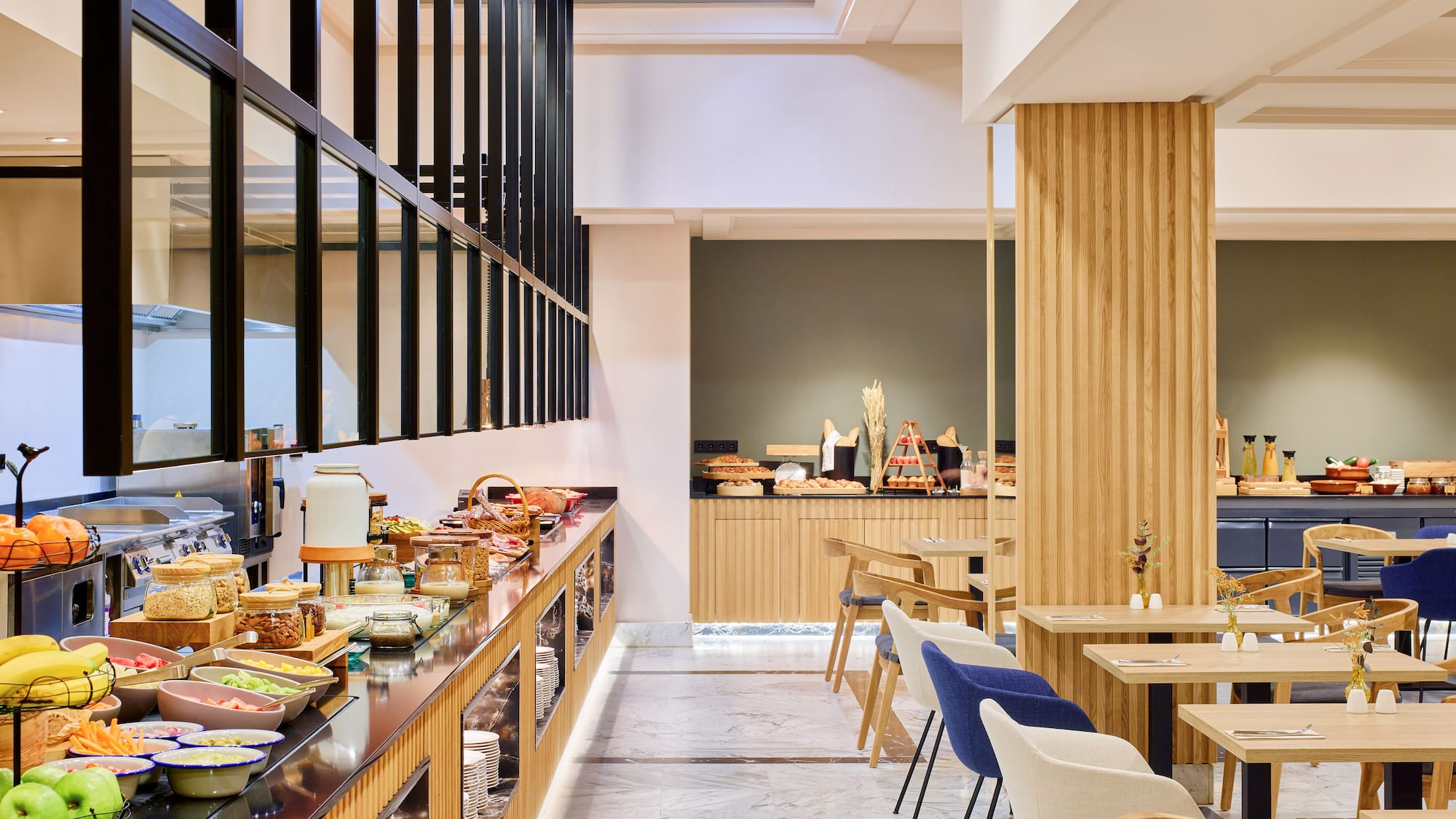 Buffet de desayuno moderno en hotel con frutas, cereales y área de mesas.