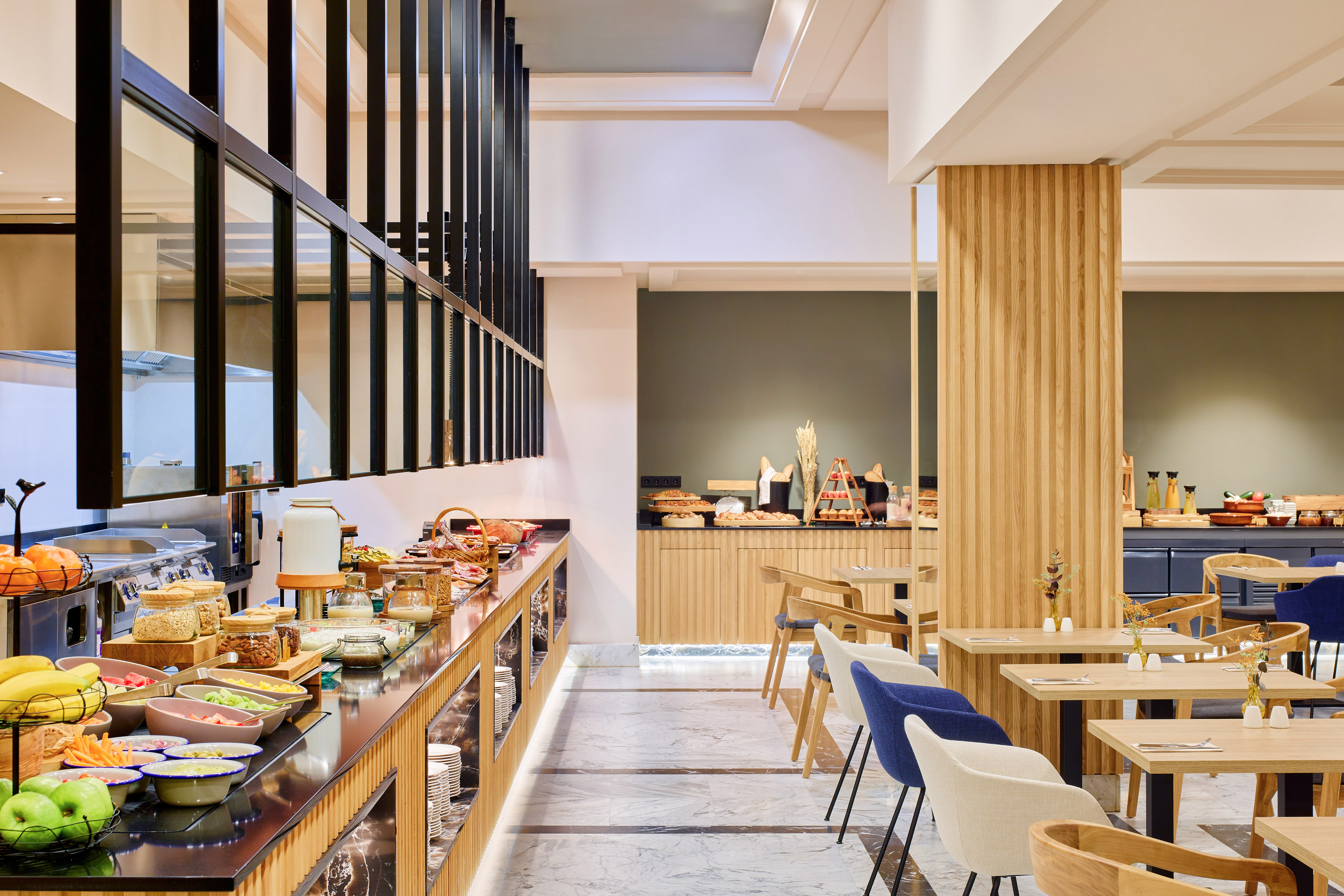 Buffet de desayuno moderno en hotel, con frutas, cereales y zona de mesas.