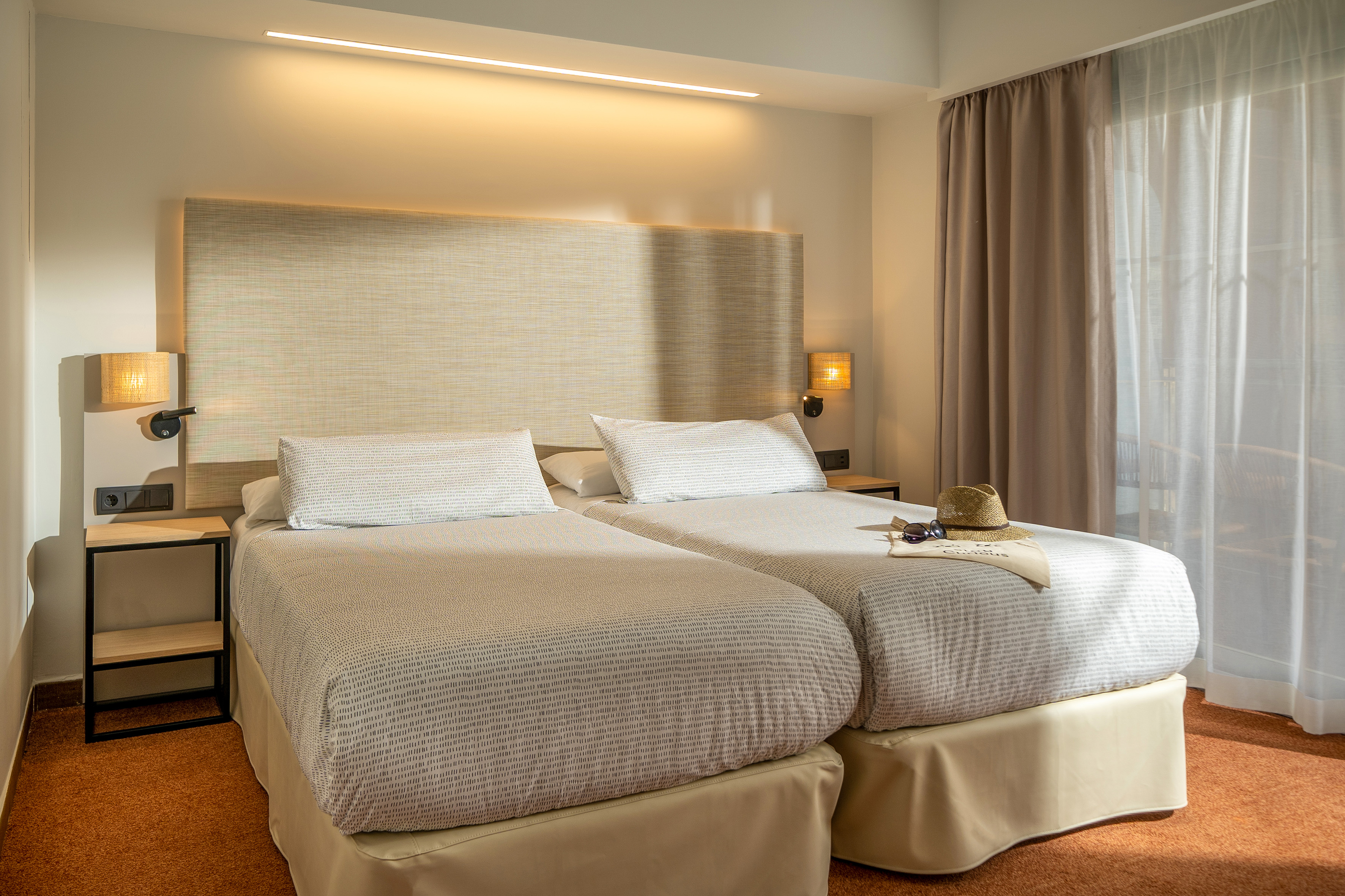Hotel guest room with two twin beds, modern lighting, and neutral decor.