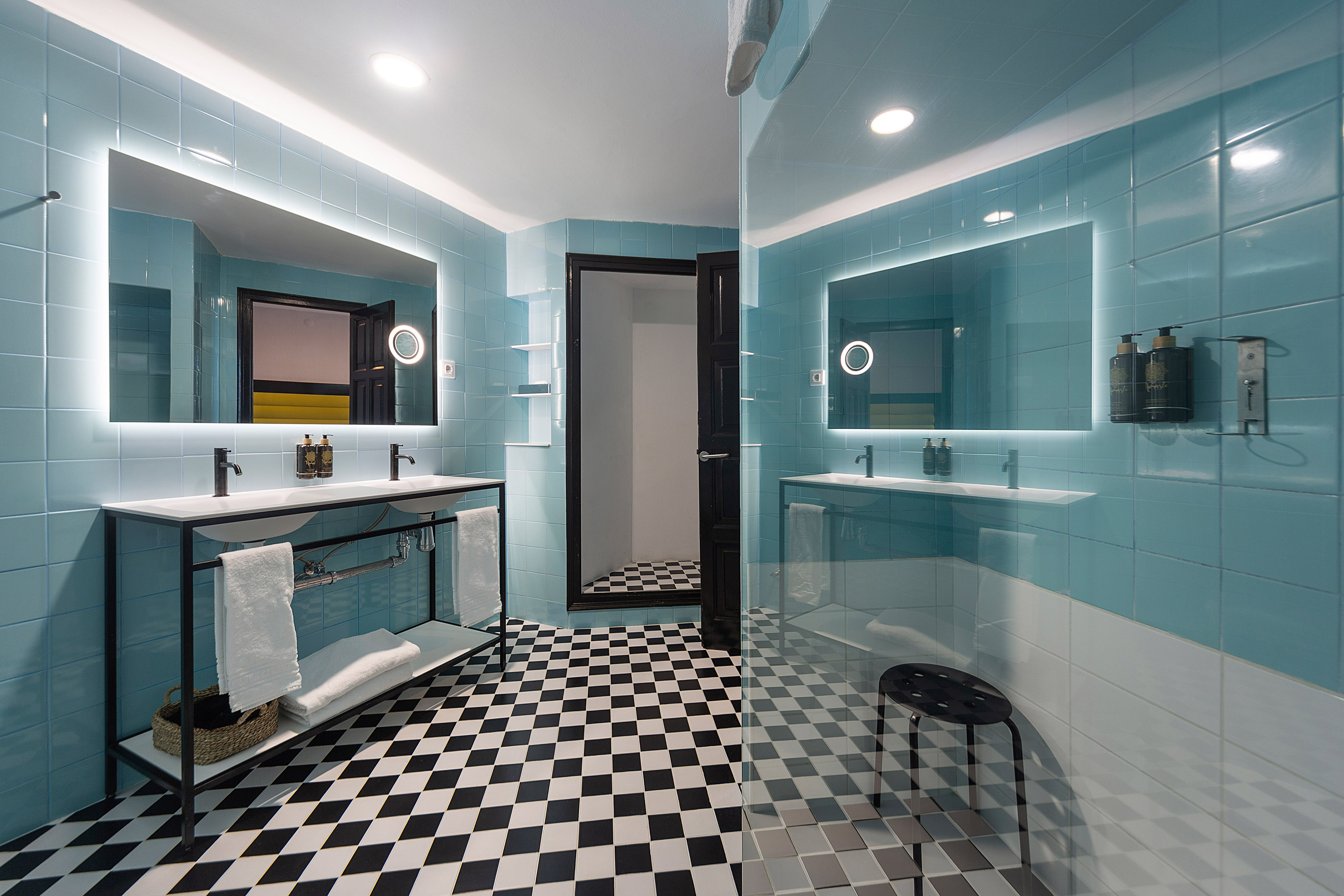 Modern bathroom with blue tiles, checkered floor, double sinks & backlit mirrors.