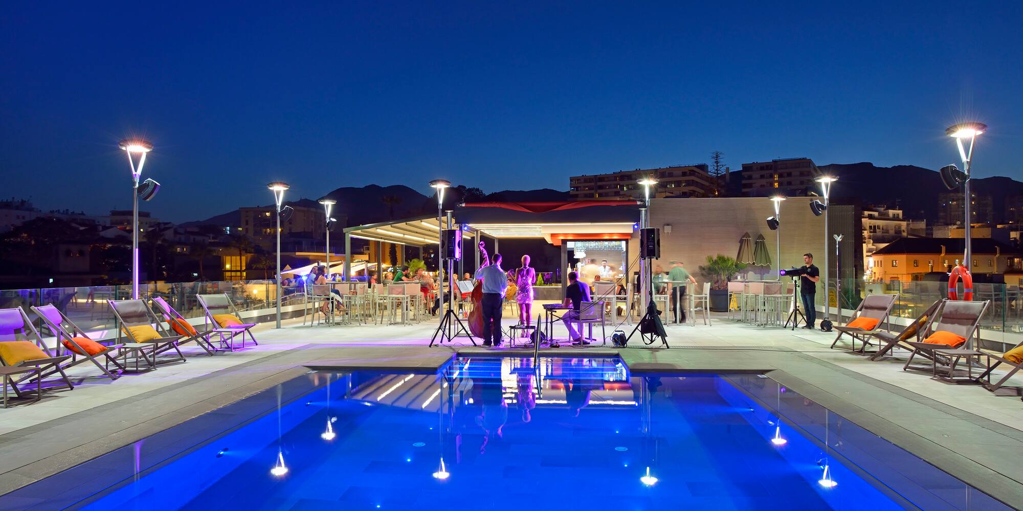 Illuminated rooftop pool and bar with live music at night.