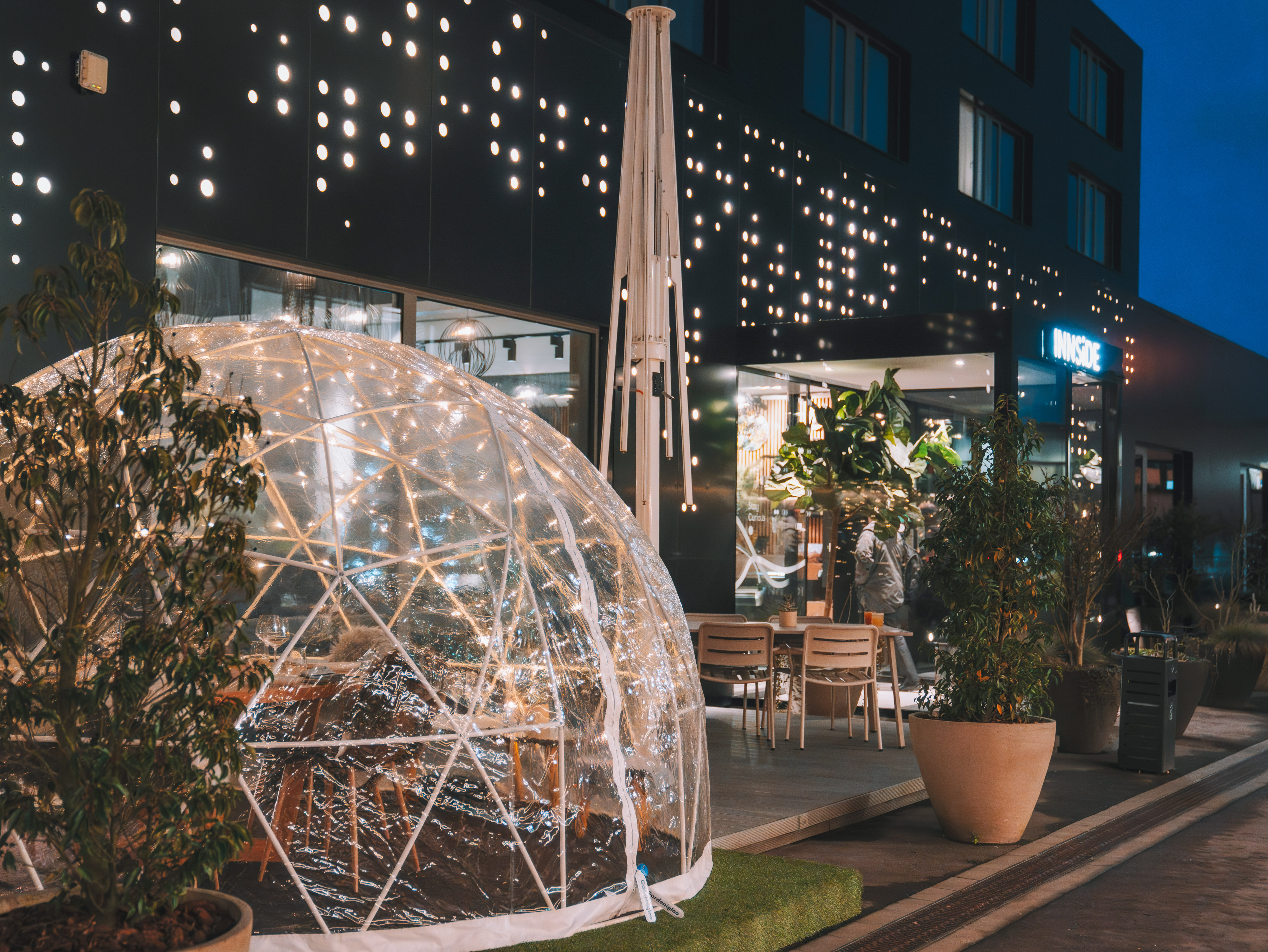 Illuminated dining igloo on modern INNSiDE hotel patio with lighted facade.