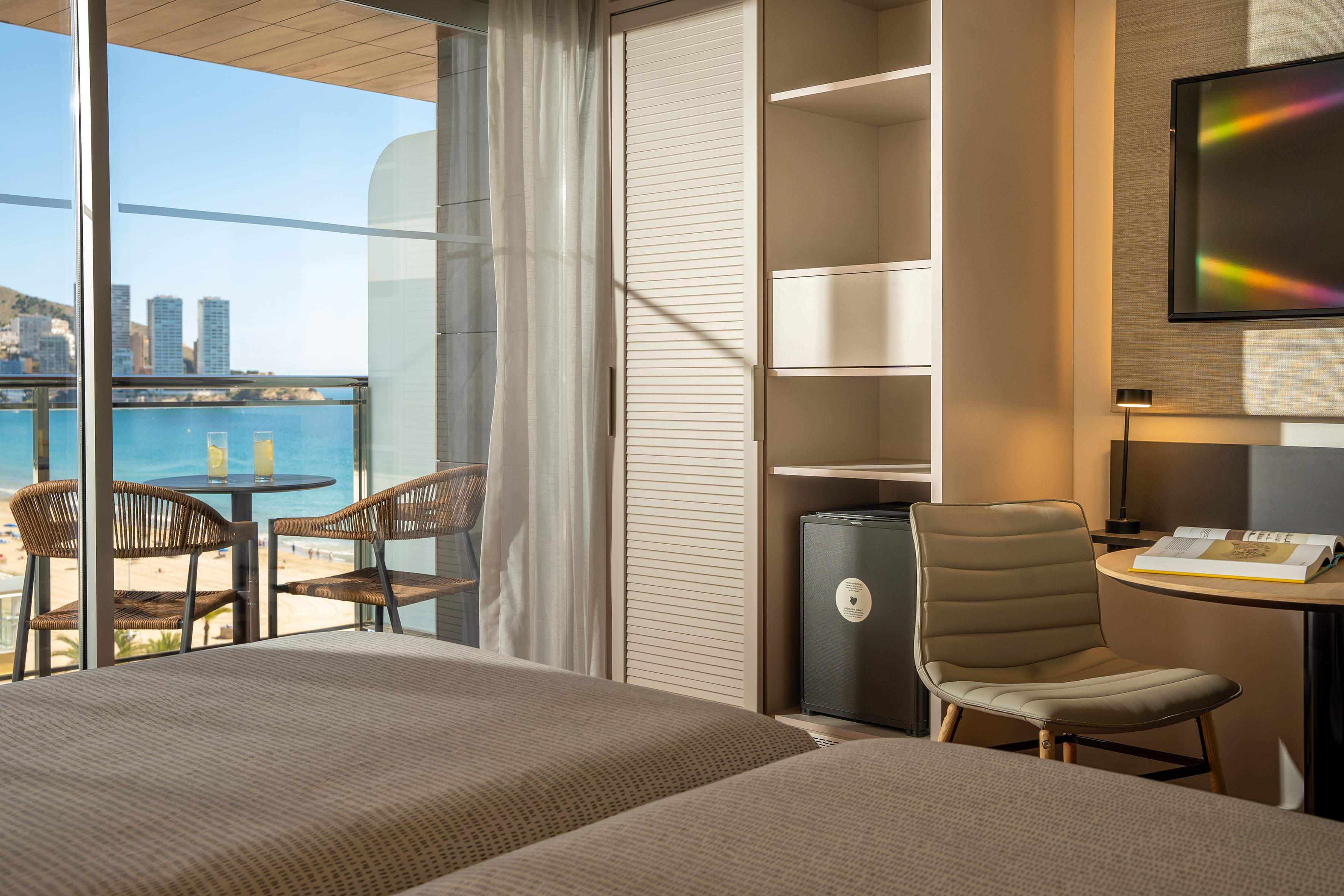Hotel room with sea view balcony, beach, and city skyline.