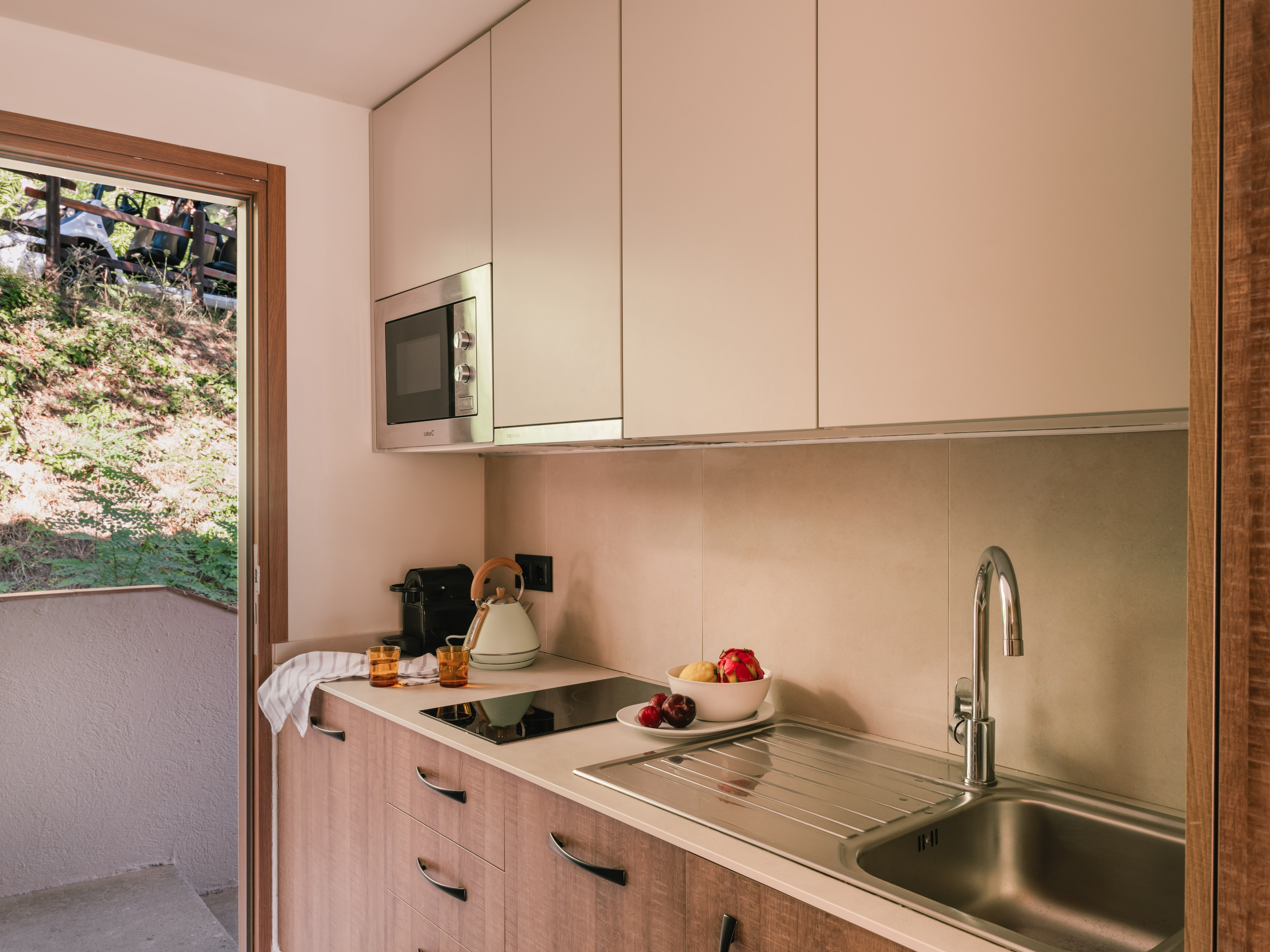 Compact modern kitchen with microwave, sink, fruit, and outdoor view.