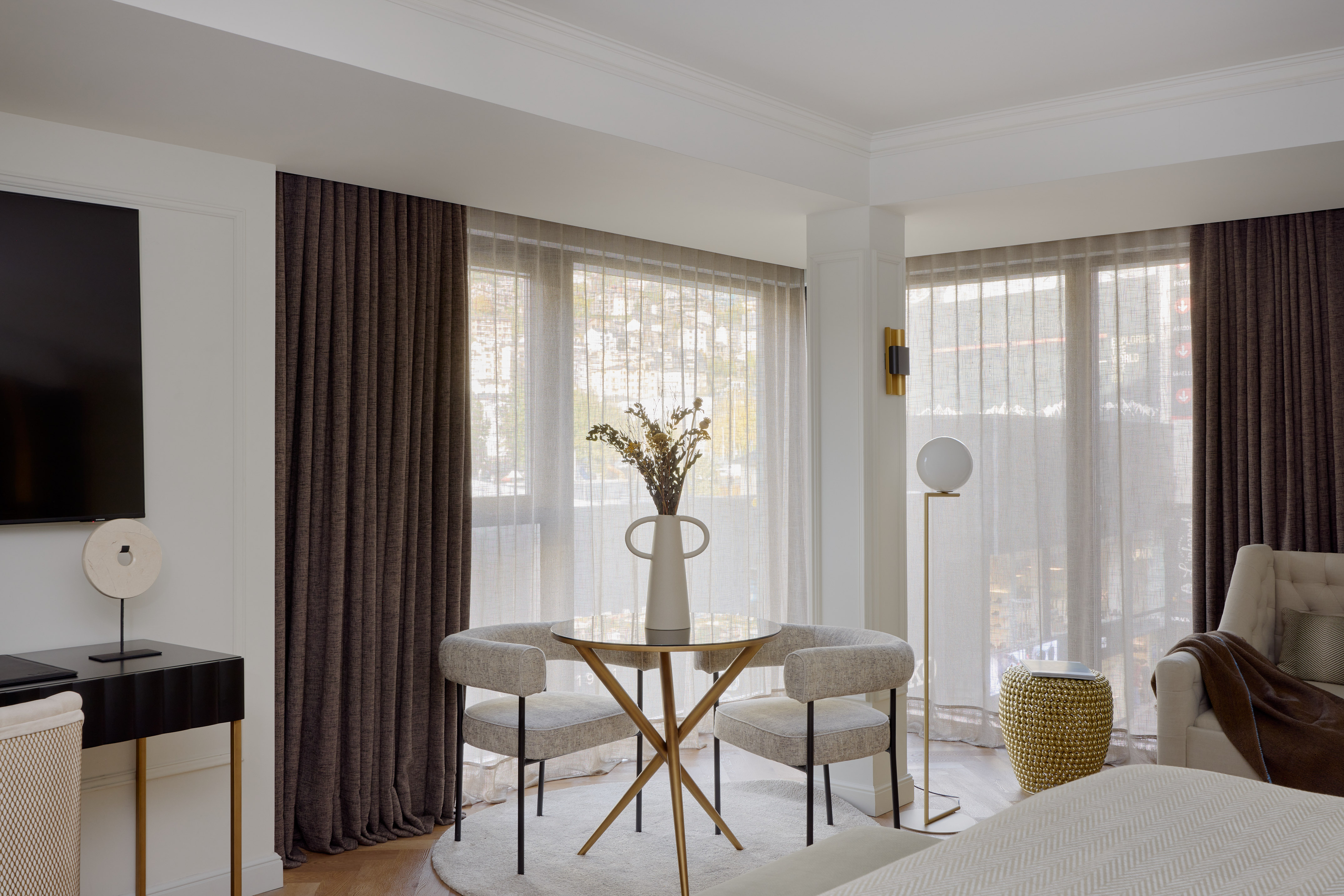 Modern interior with small round table, two chairs, vase, and sheer curtains.