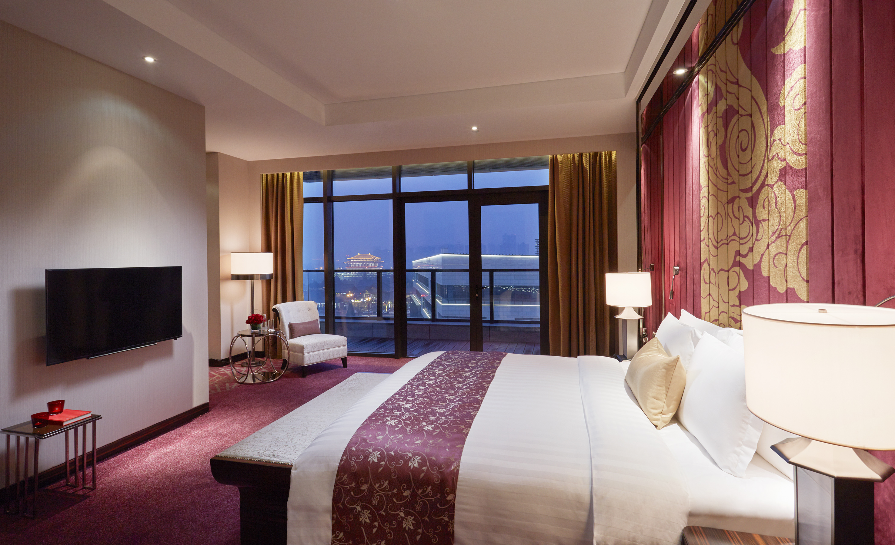 Modern luxury hotel room with city skyline view and stylish red & gold decor.