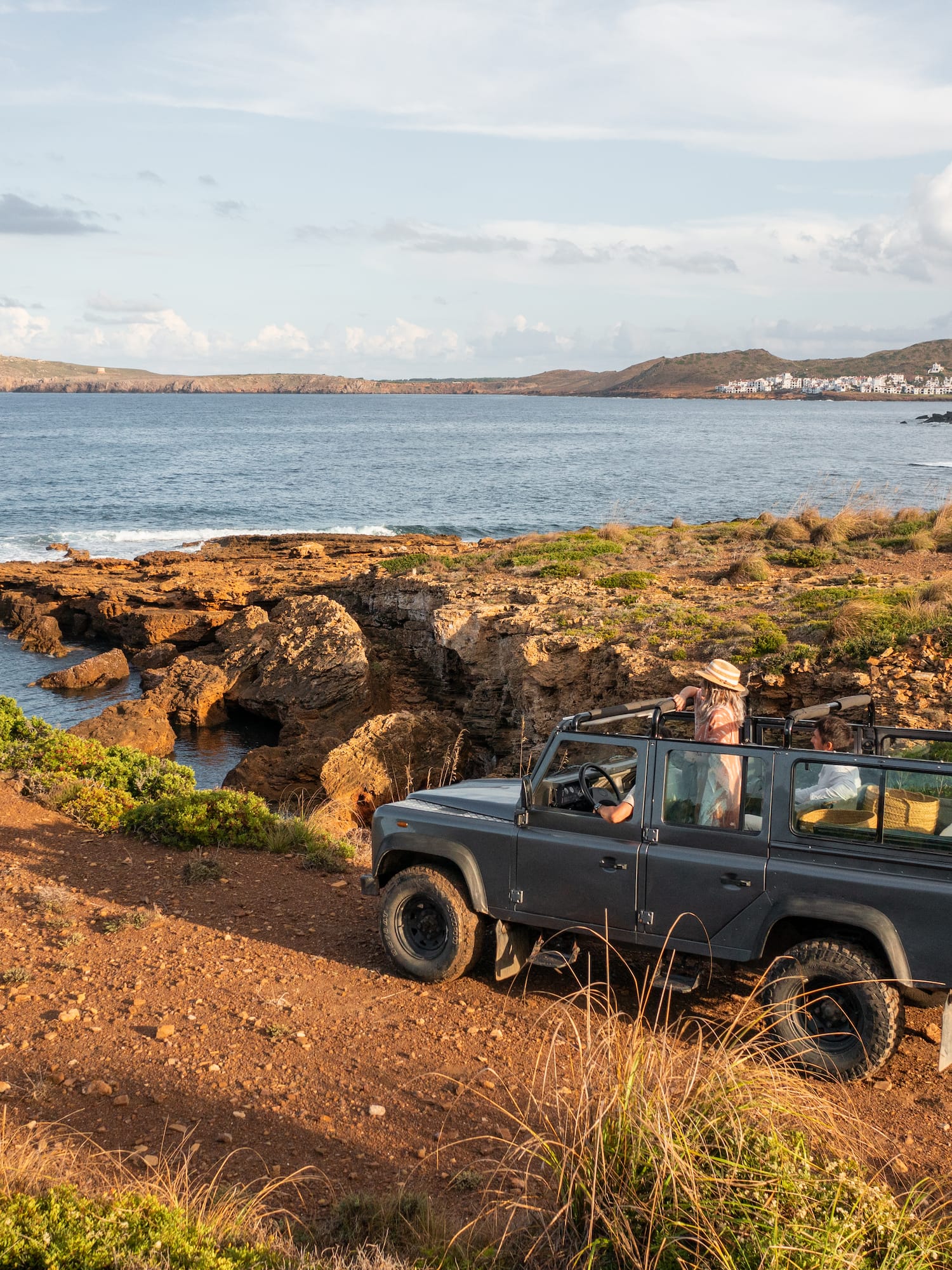 Grey 4x4 on a rocky coastal track, Mediterranean sea, distant village.