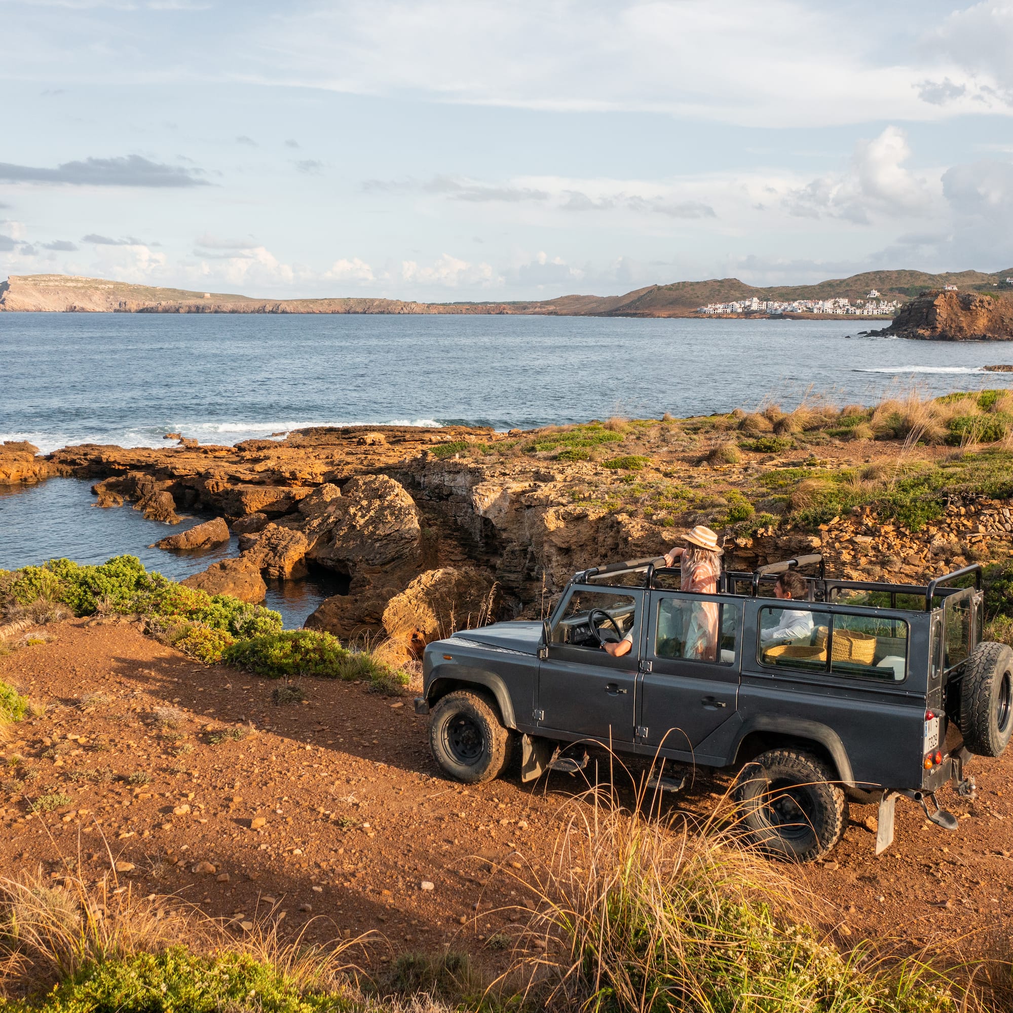 Grey 4x4 on a rocky coastal track, Mediterranean sea, distant village.