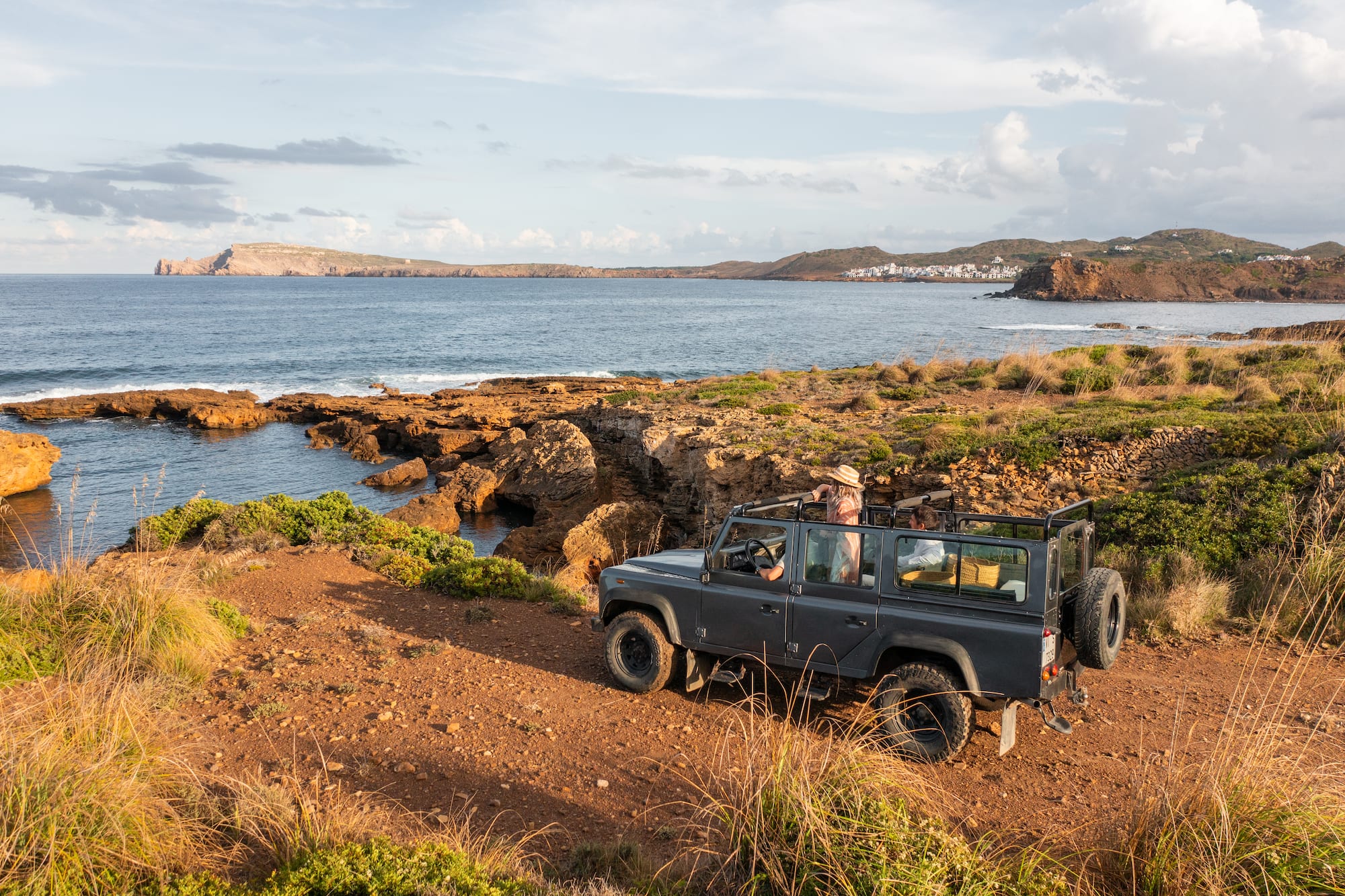Grey 4x4 on a rocky coastal track, Mediterranean sea, distant village.
