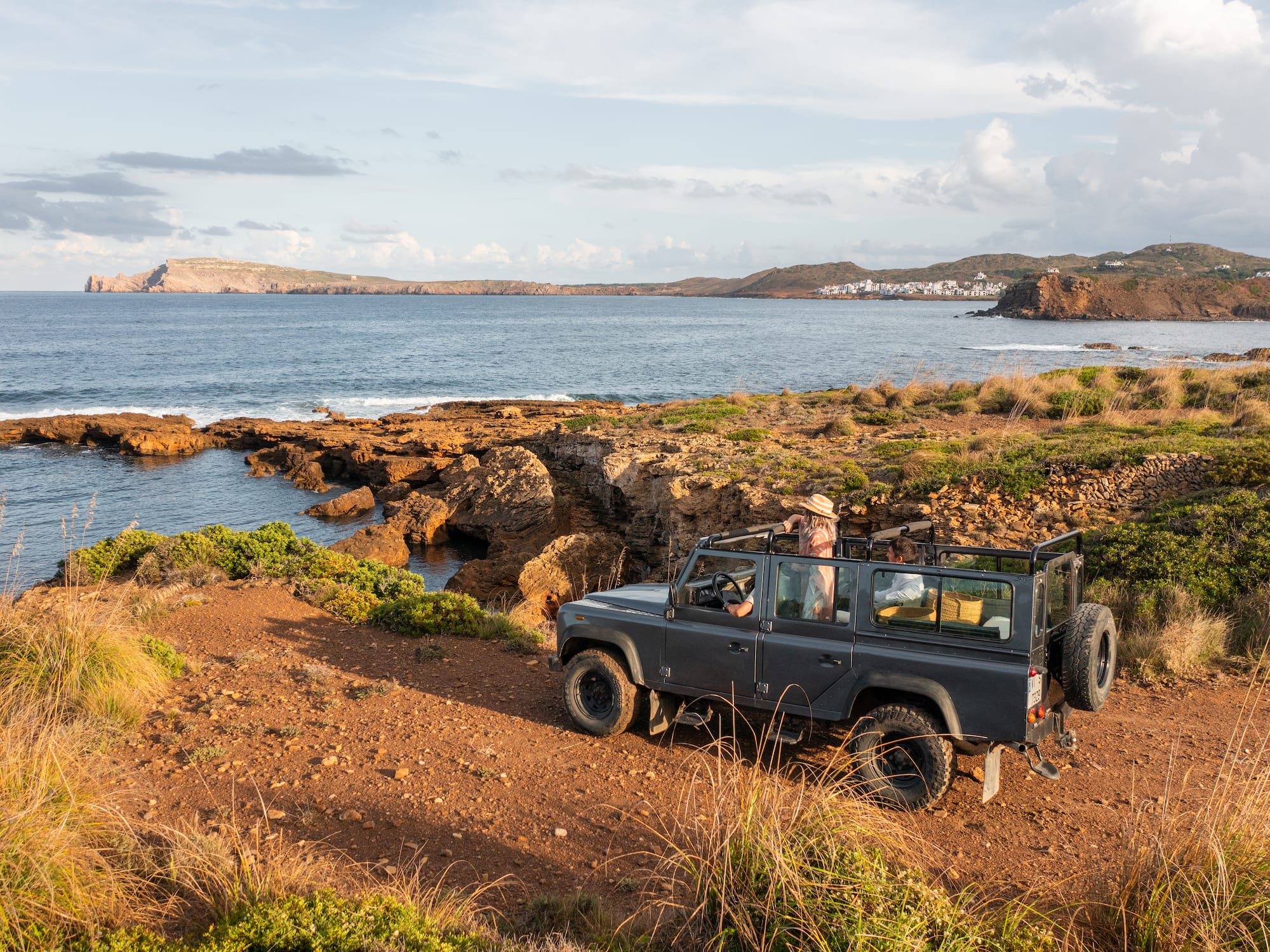 Grey 4x4 on a rocky coastal track, Mediterranean sea, distant village.