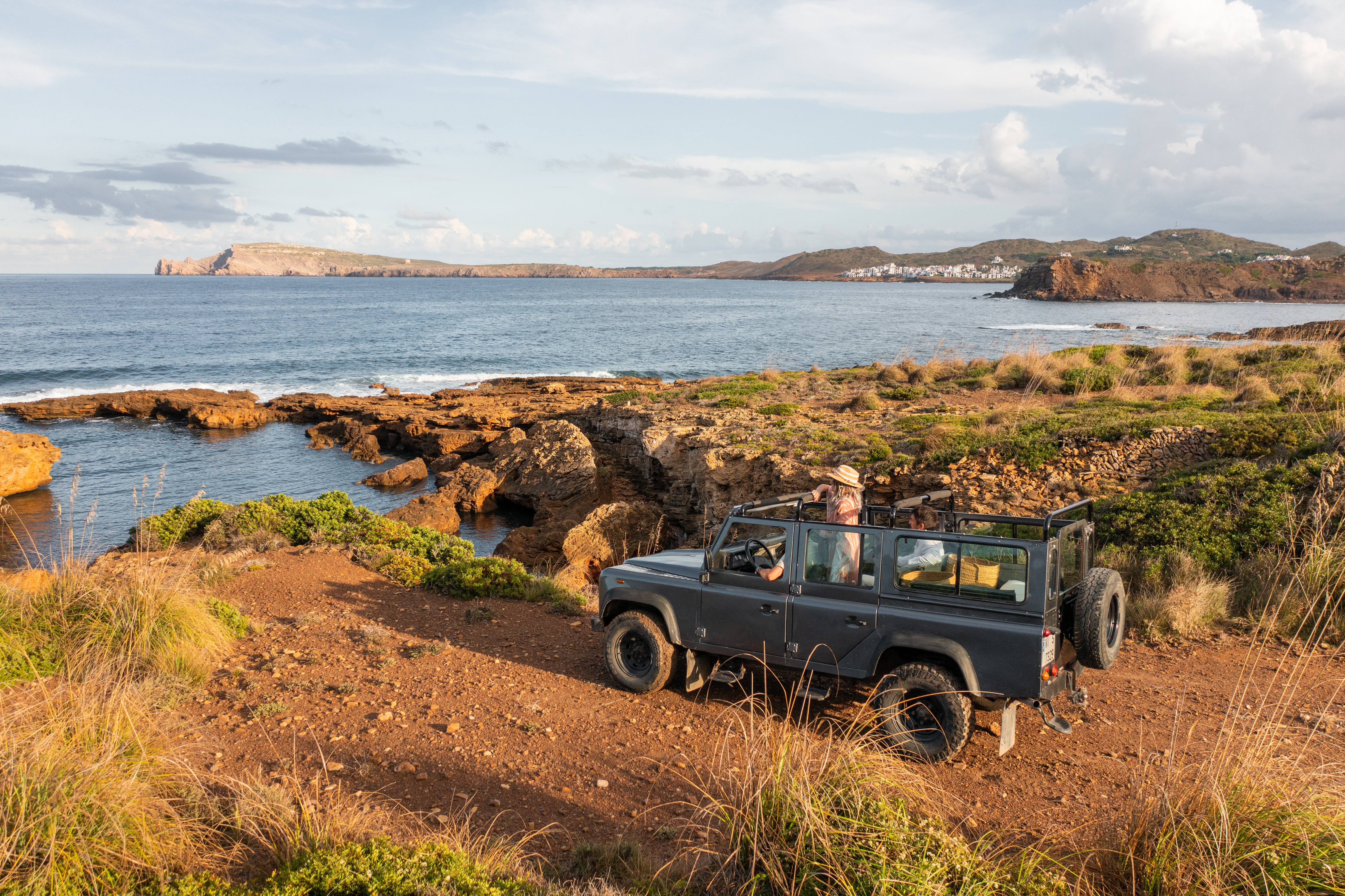 Grey 4x4 on a rocky coastal track, Mediterranean sea, distant village.