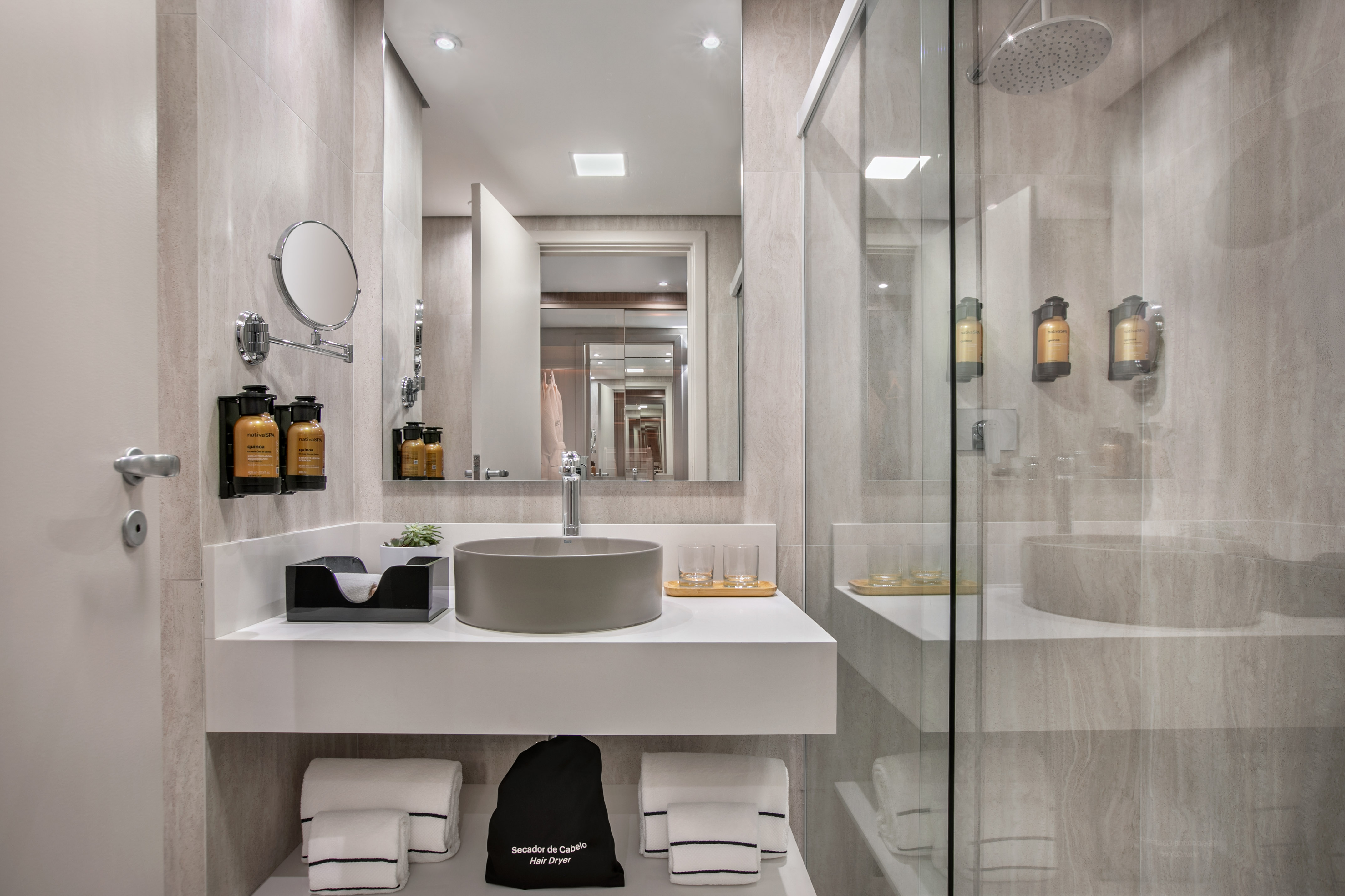 Modern hotel bathroom with gray vessel sink, large mirror, and glass shower.