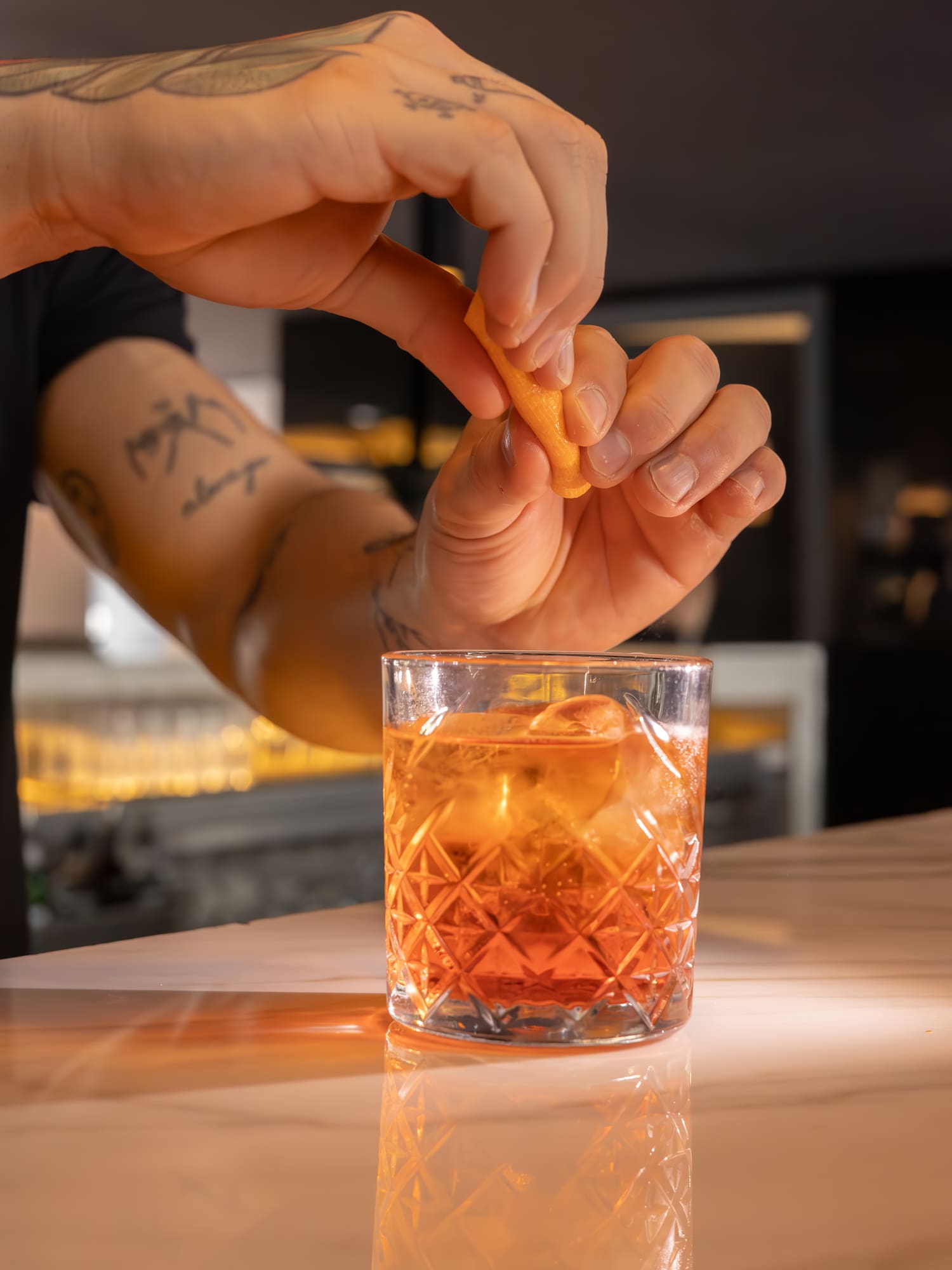 Bartender garnishing an orange cocktail with an orange peel on a bar.