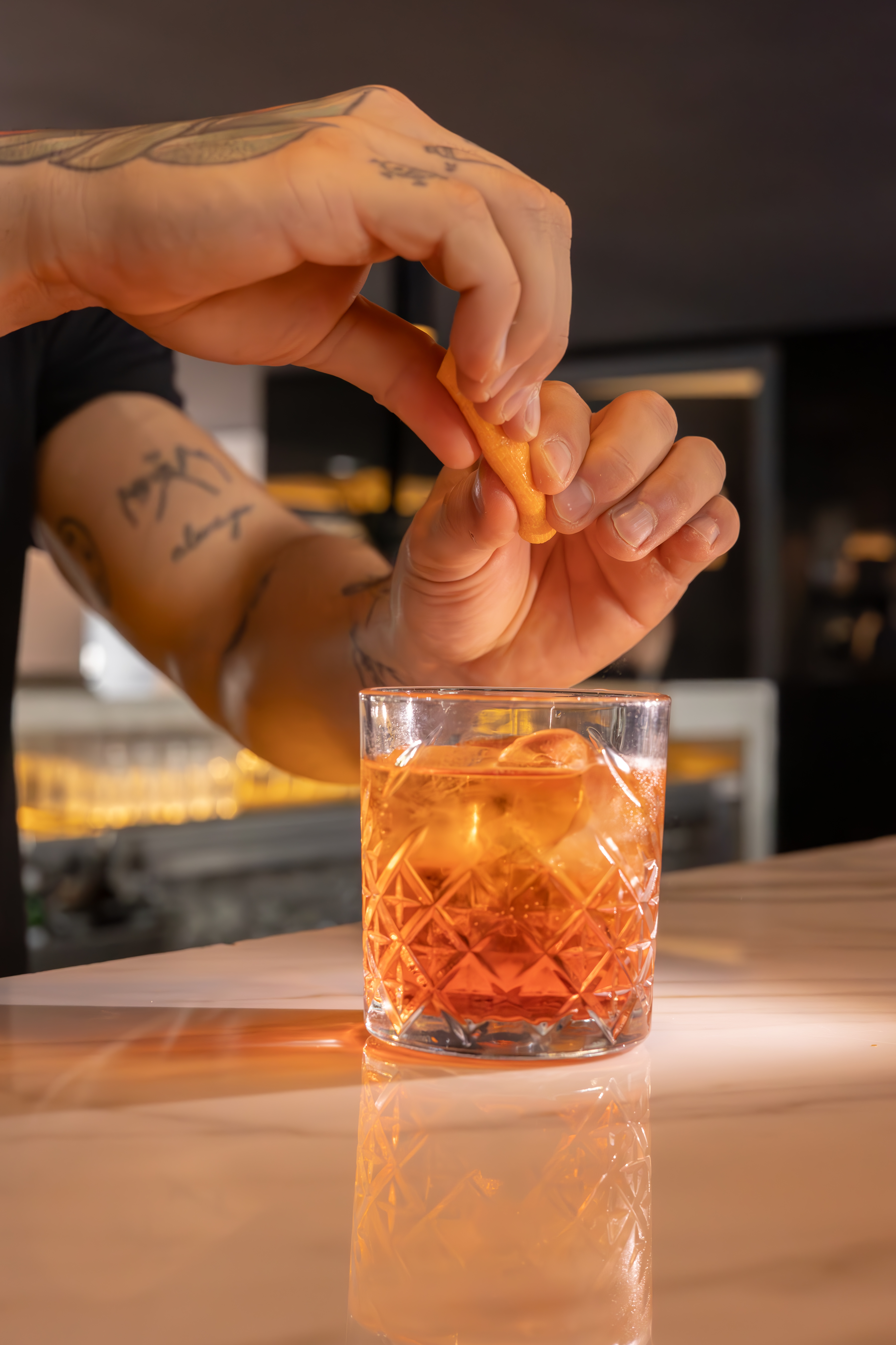Bartender garnishing an orange cocktail with an orange peel on a bar.
