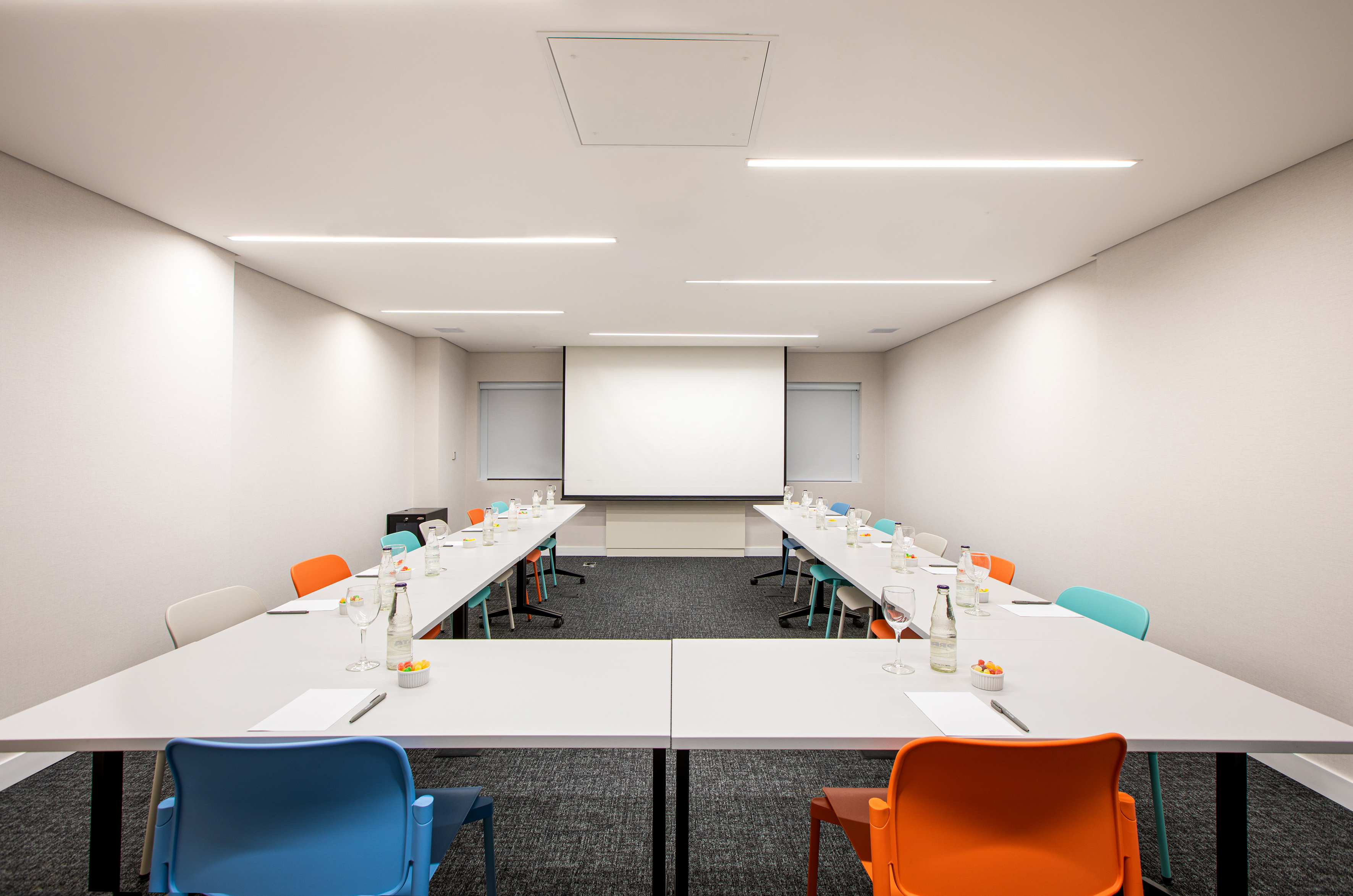 Modern U-shaped conference room with projector screen and colorful chairs.