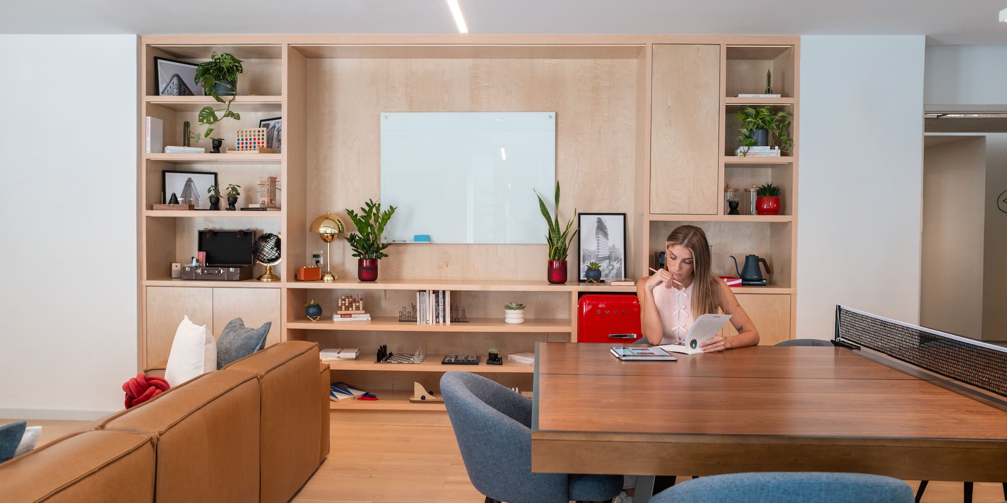 Woman reading at multi-use ping-pong table in modern office lounge.