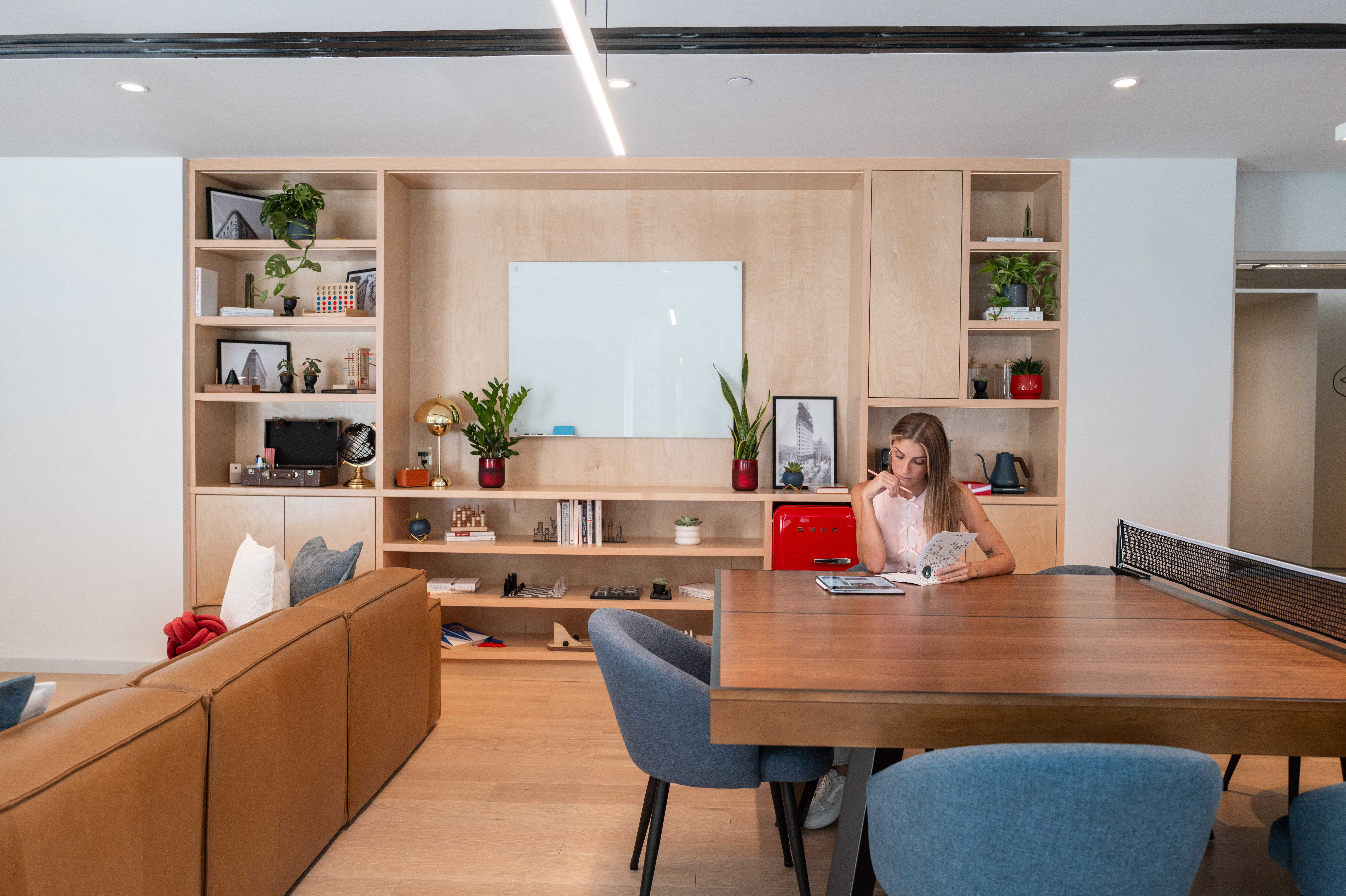 Woman reading at multi-use ping-pong table in modern office lounge.