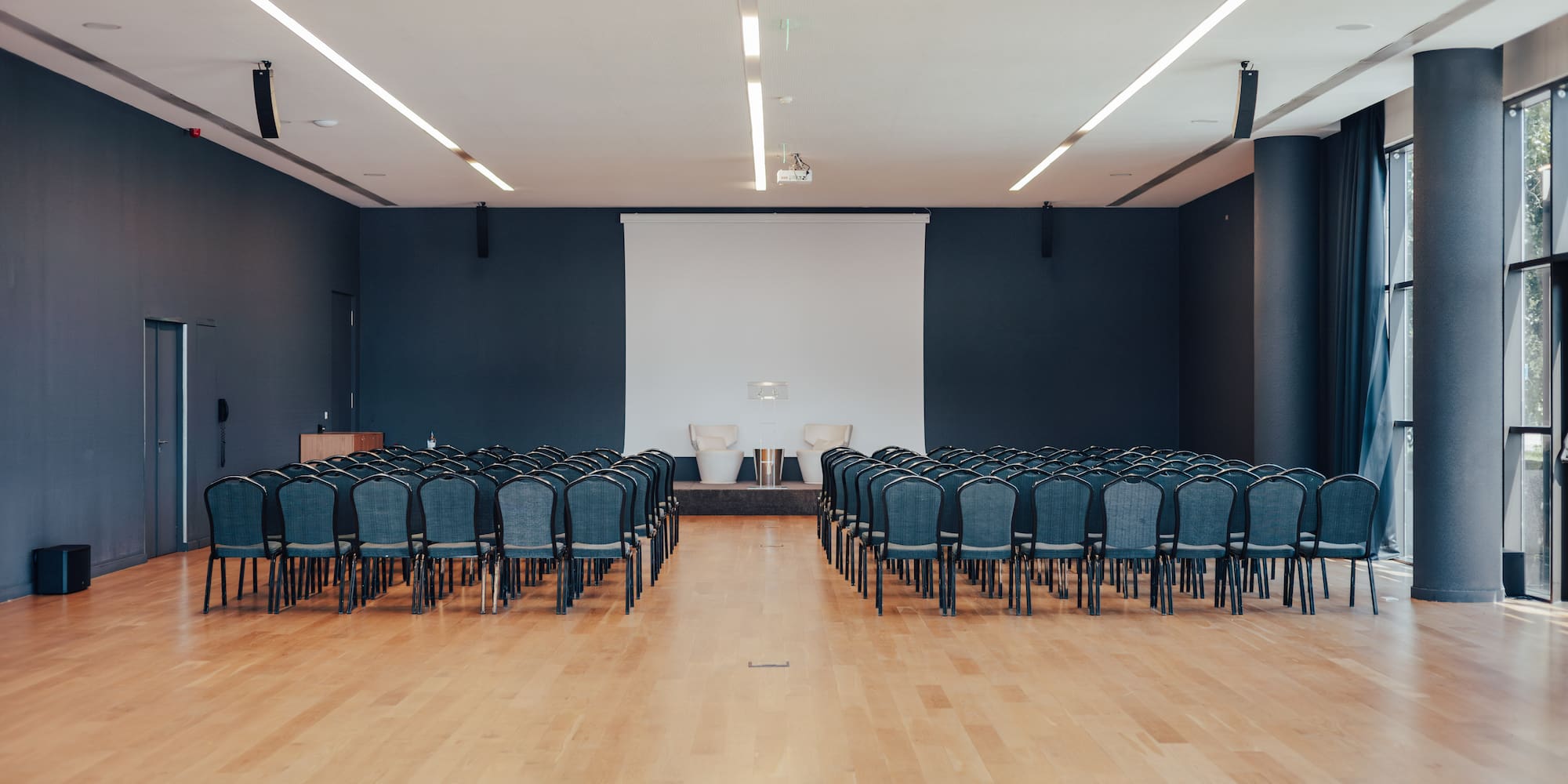 Empty modern conference hall with blue chairs, screen, and podium.