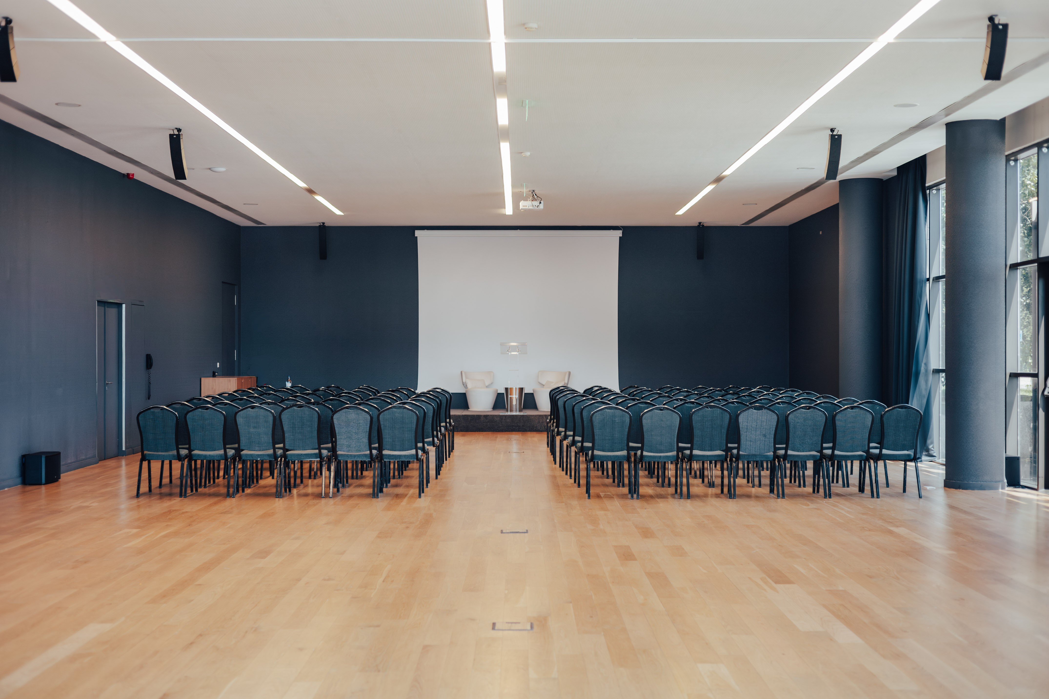 Empty modern conference hall with blue chairs, screen, and podium.