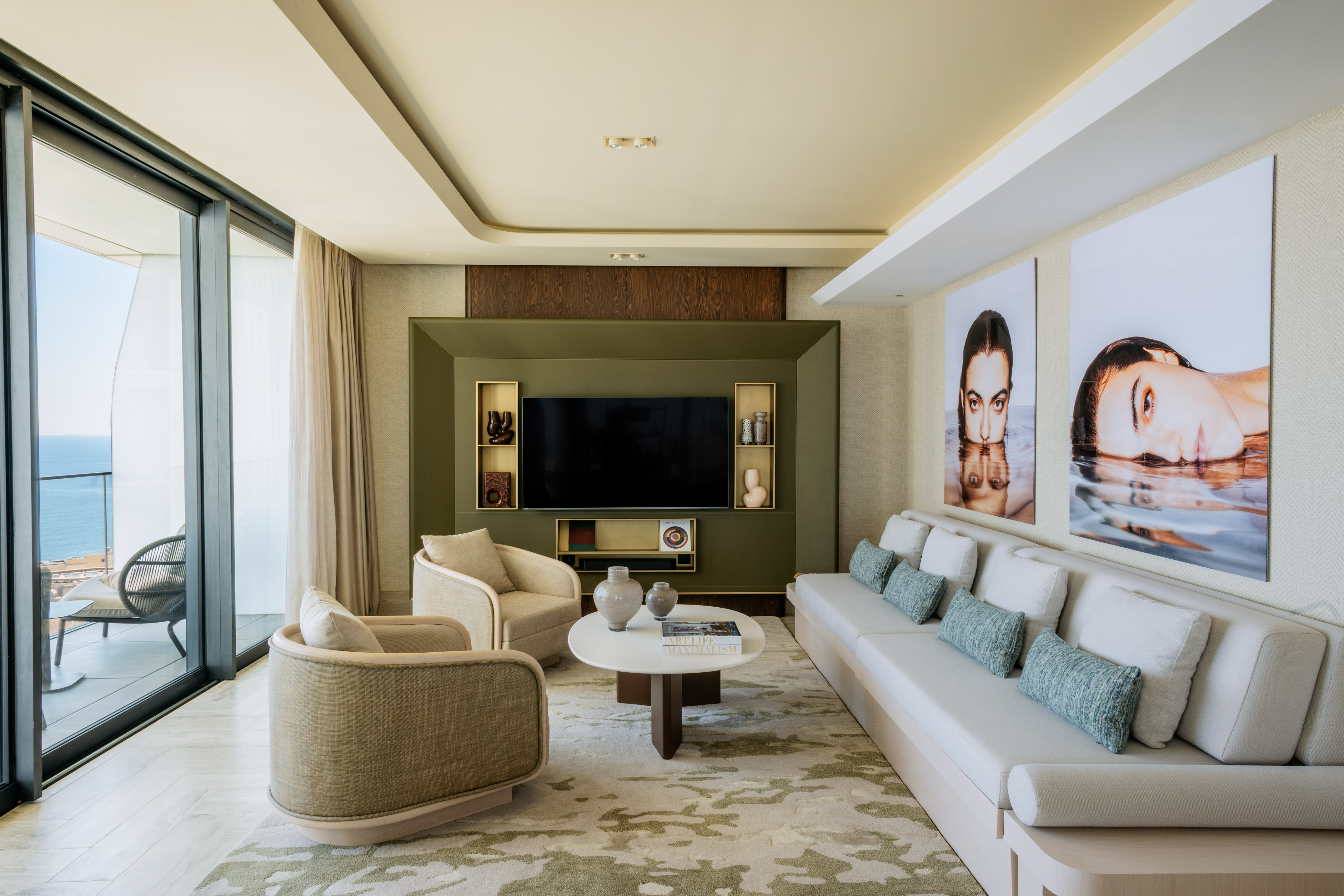 Modern living room with ocean view, olive green TV wall, and contemporary art prints.