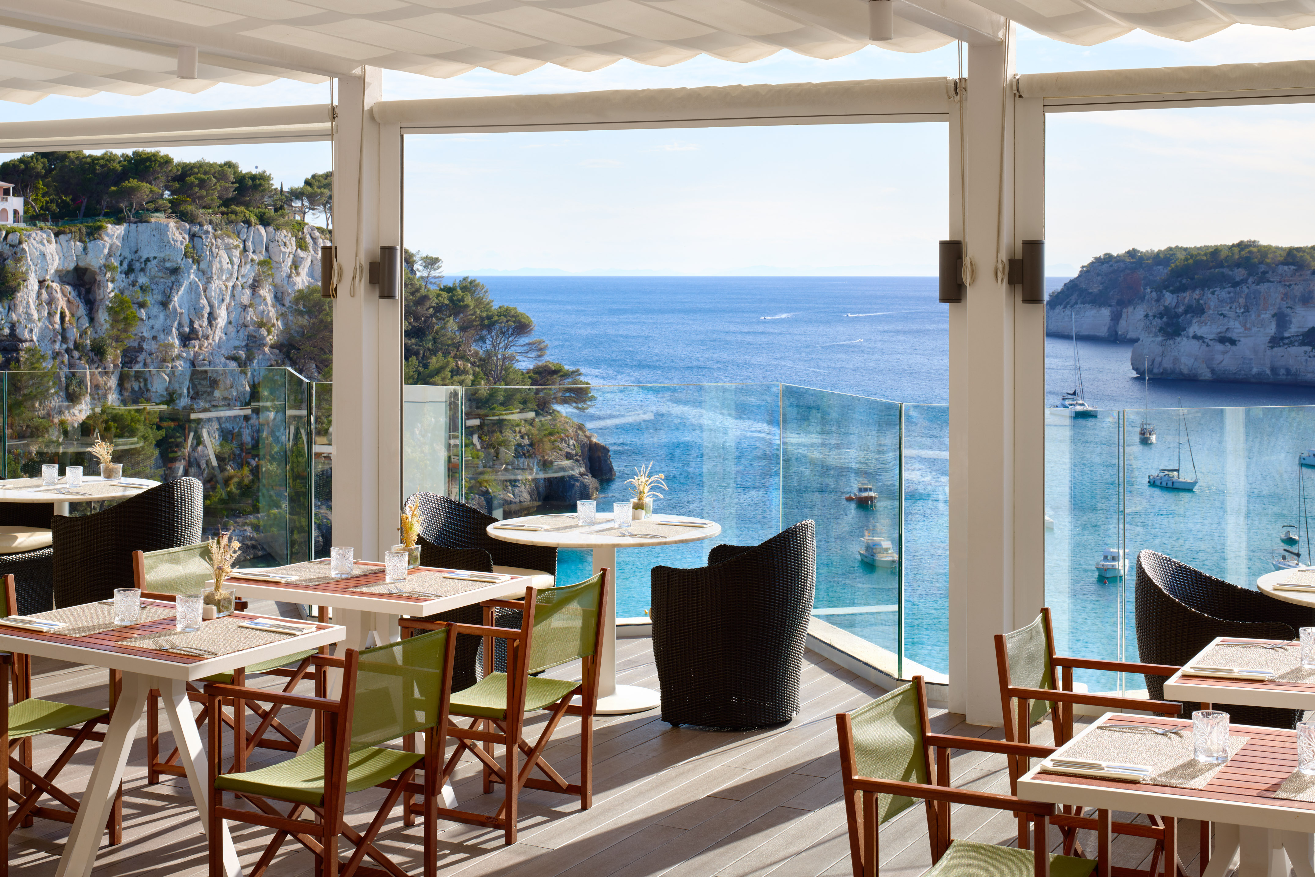 Restaurant terrace with panoramic sea view, boats, and coastal cliffs.