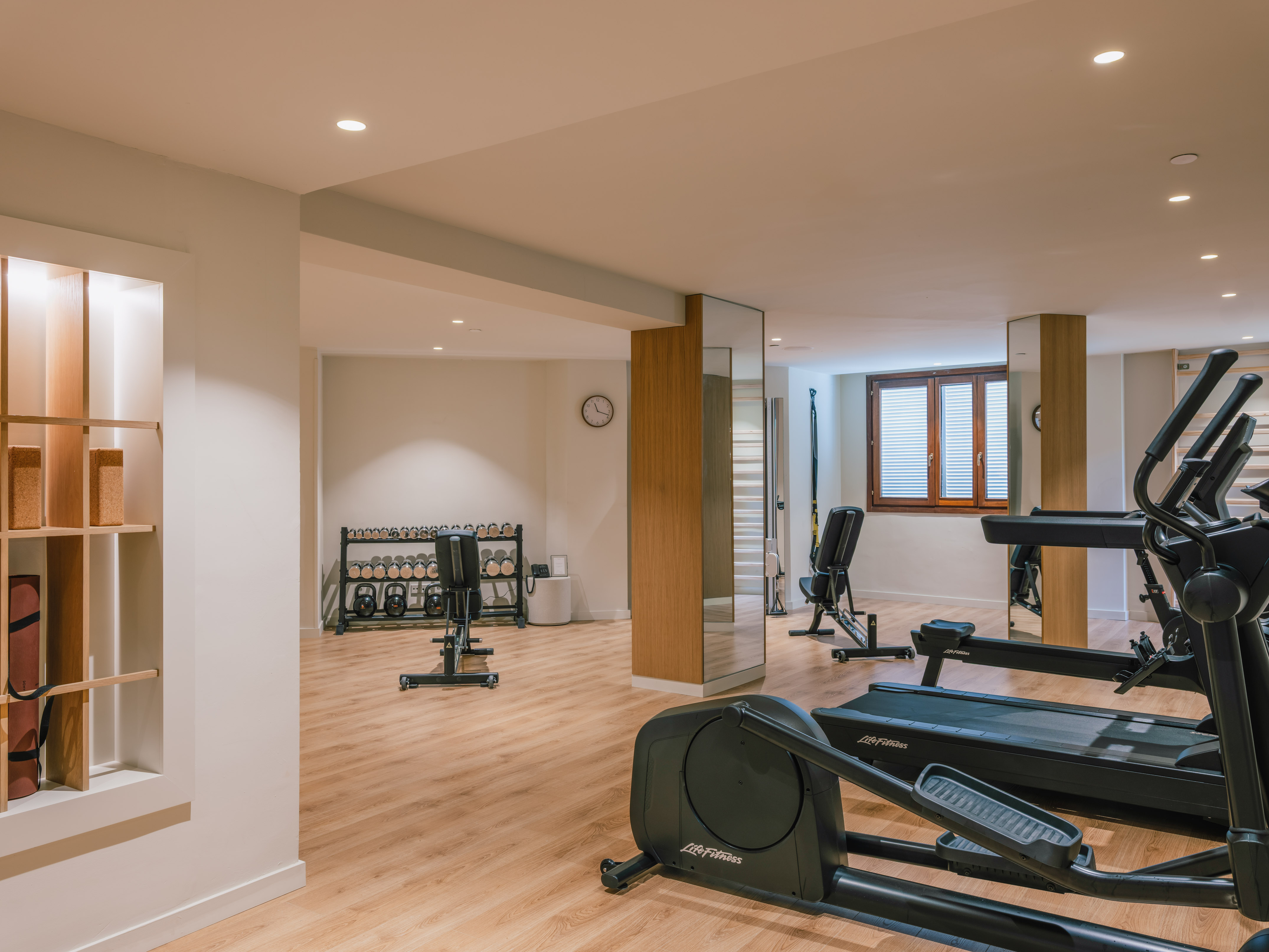 Modern gym with cardio machines, weights, and yoga equipment on a wooden floor.