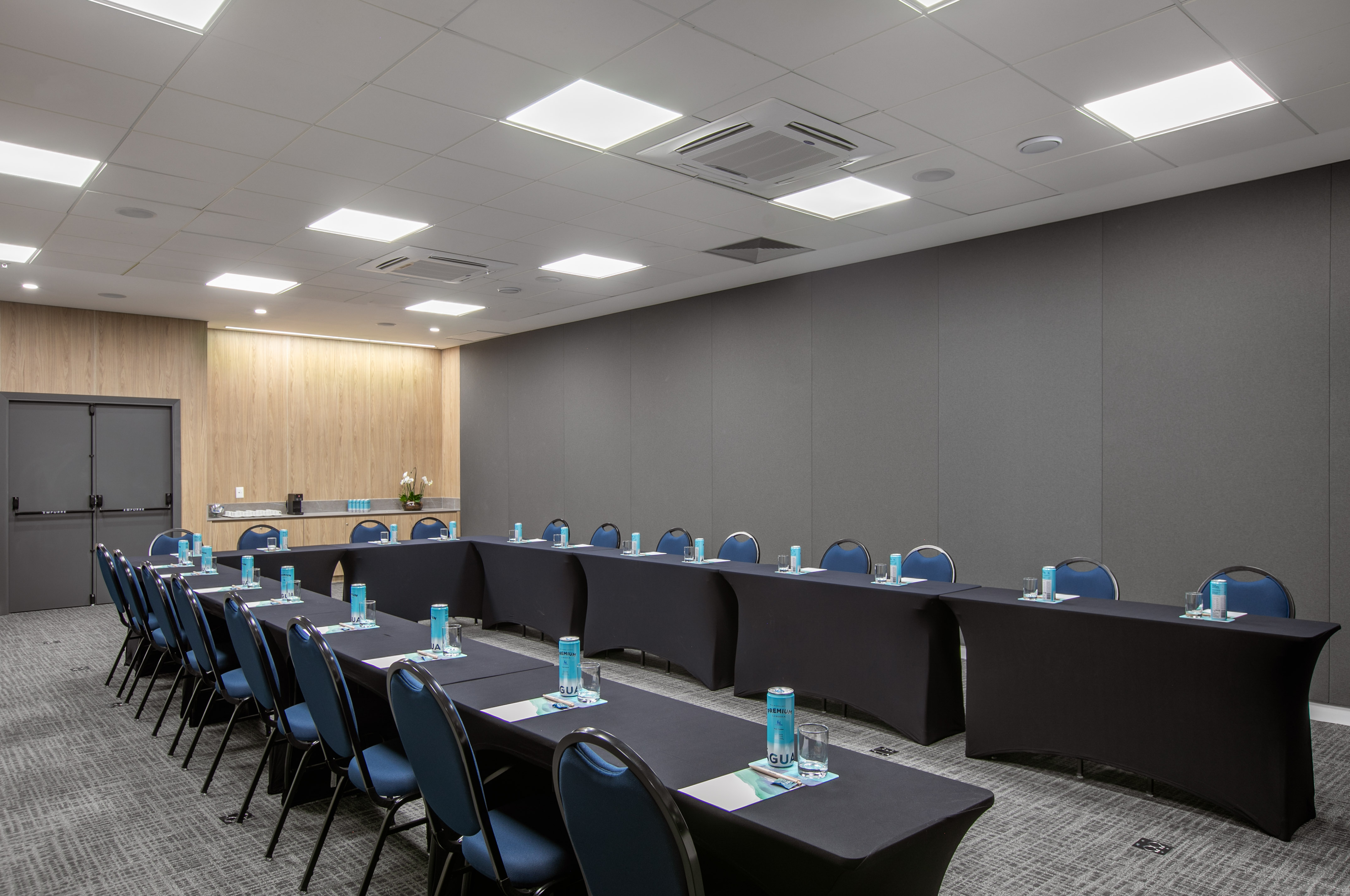 U-shaped meeting room with blue chairs, black tables, and refreshments.