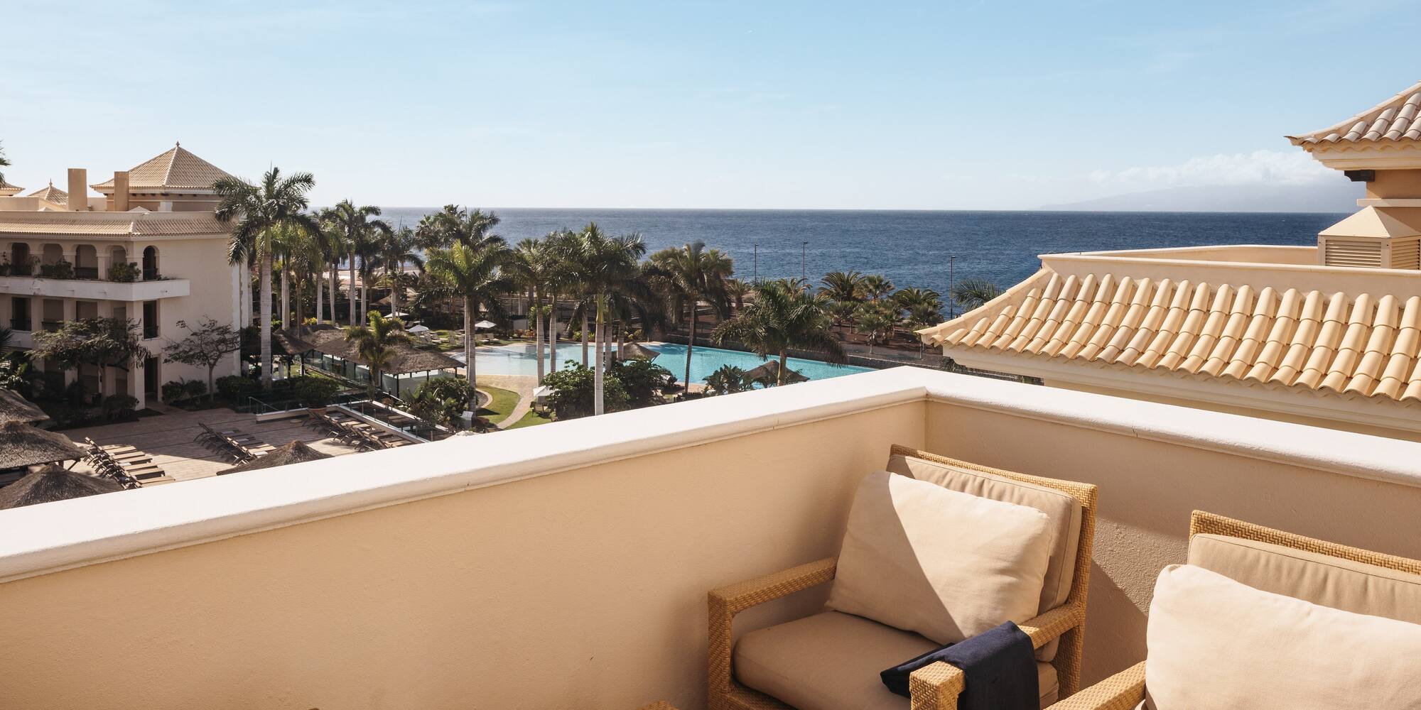 a balcony with chairs and a pool overlooking the ocean