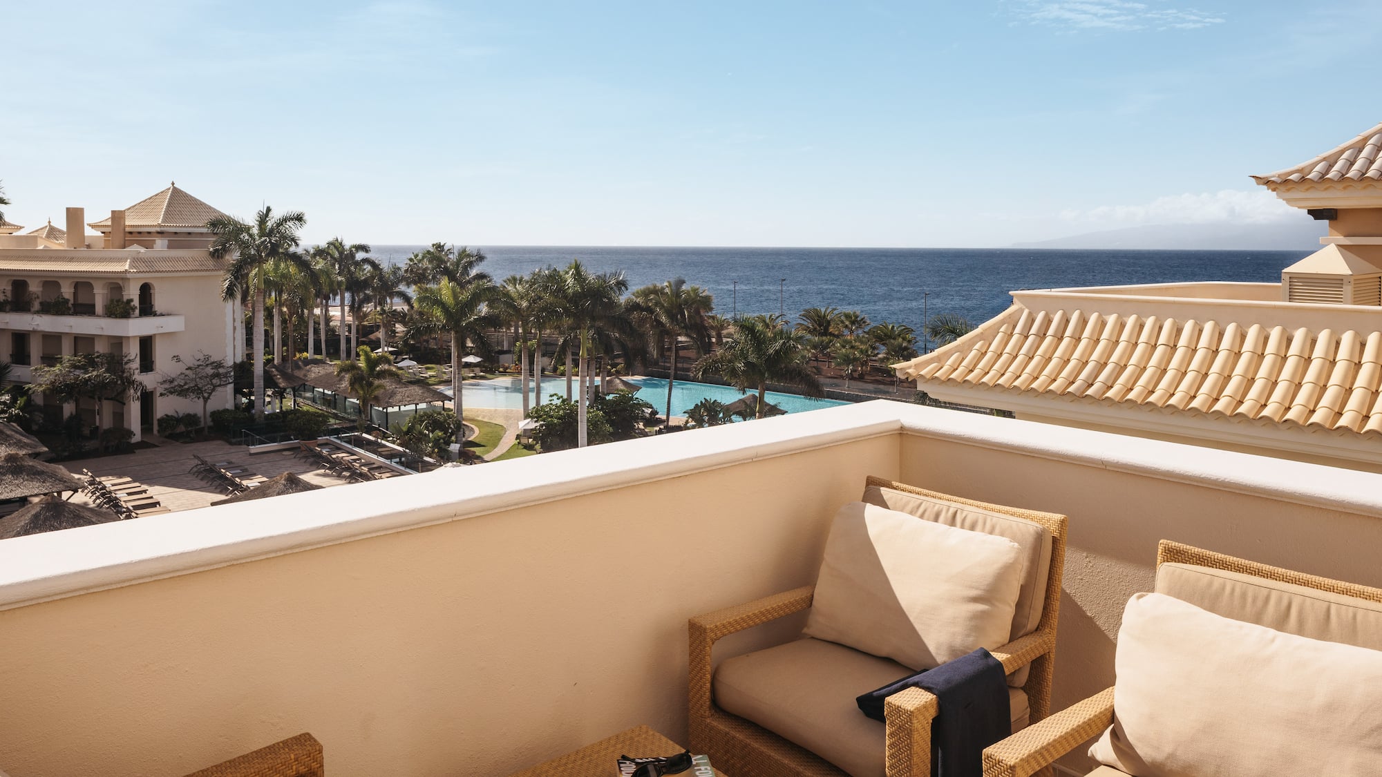 a balcony with chairs and a pool overlooking the ocean
