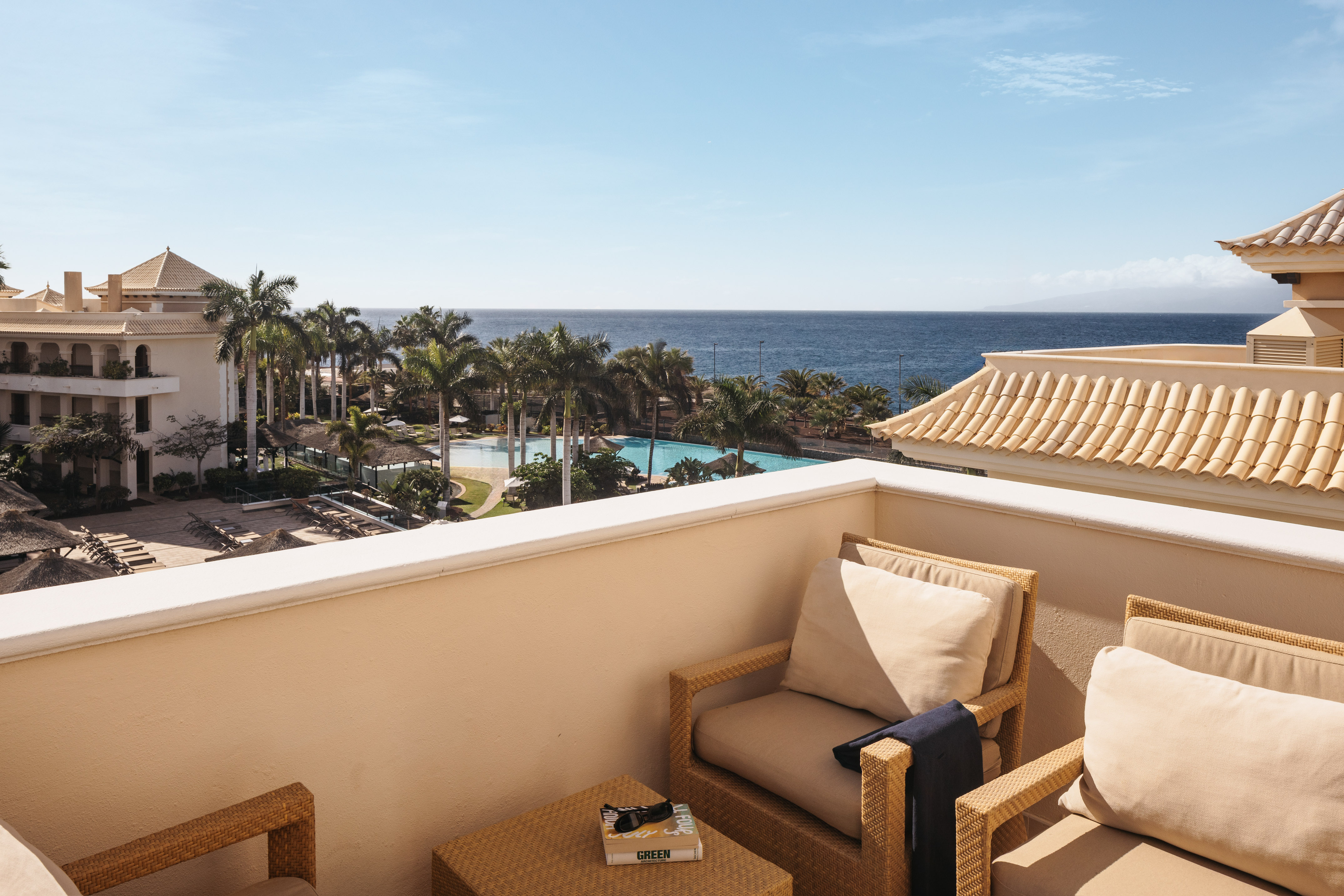 Resort balcony with ocean, palm trees, and swimming pool view.