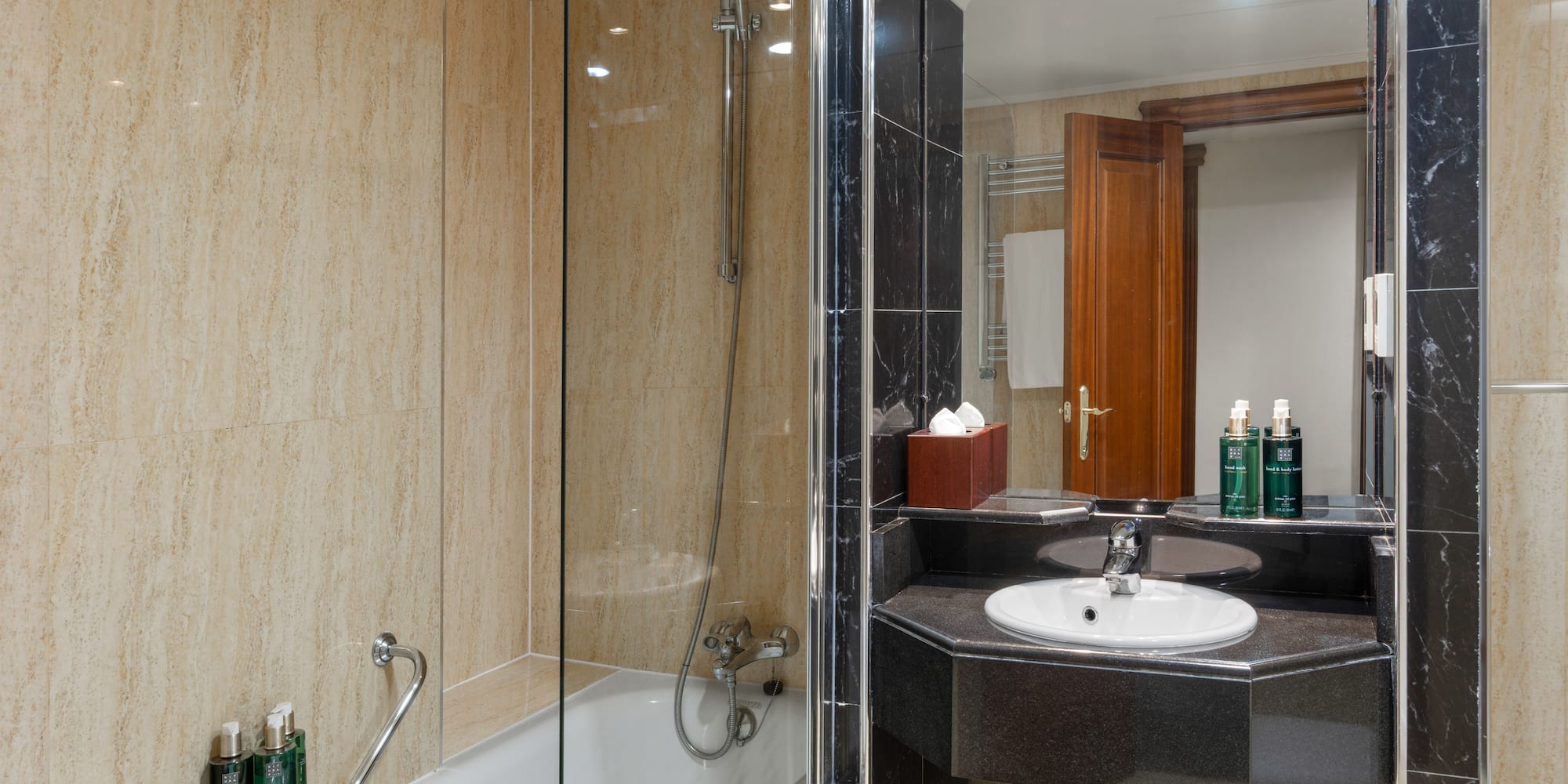 Modern hotel bathroom with shower, bathtub, black marble vanity, beige tiles.