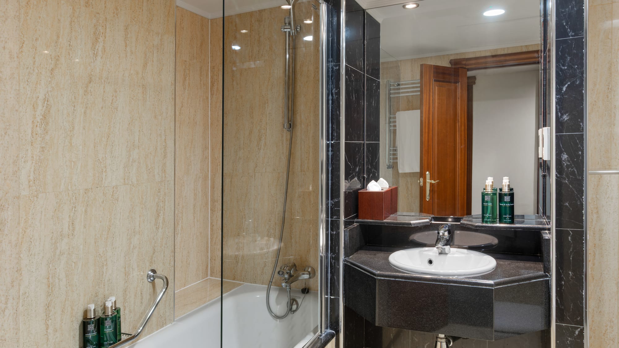 Modern hotel bathroom with shower, bathtub, black marble vanity, beige tiles.