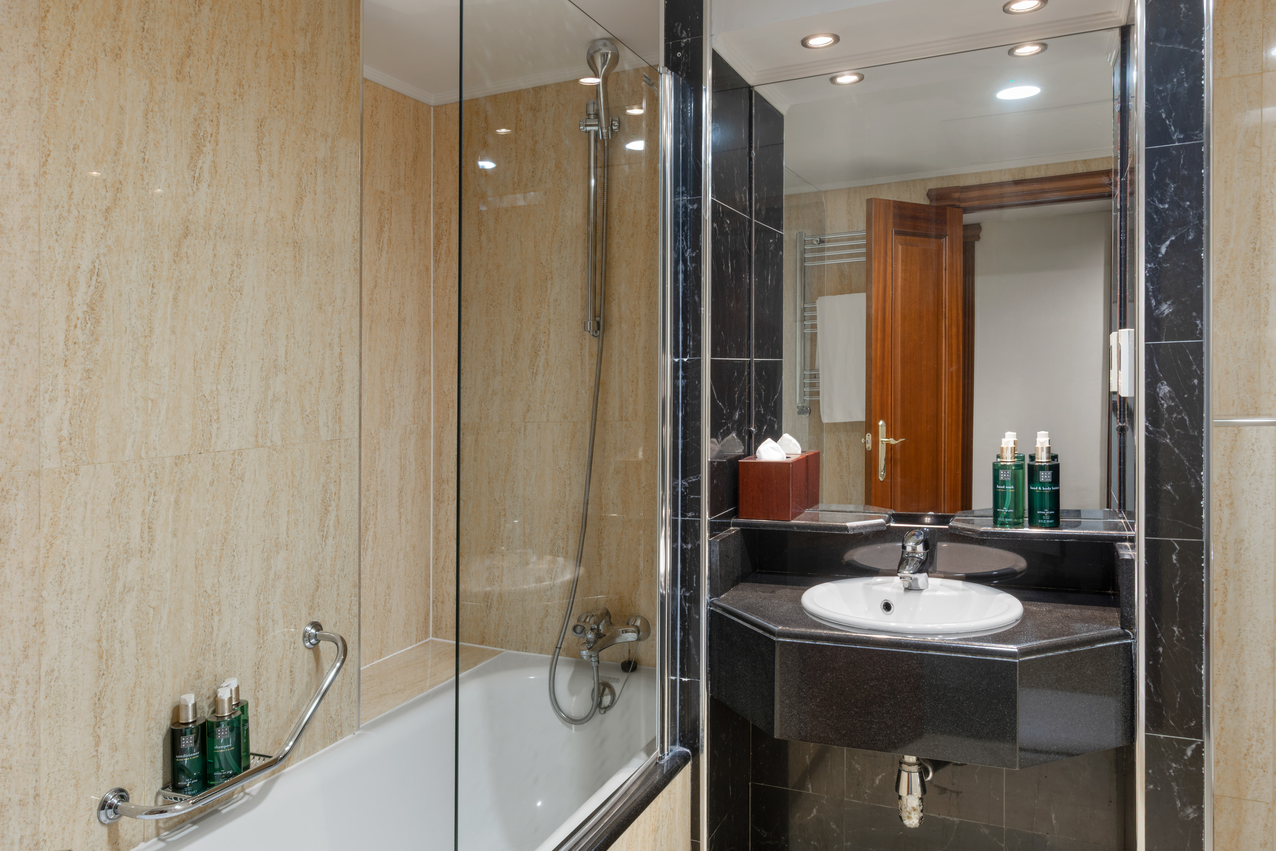 Modern hotel bathroom with shower, bathtub, black marble vanity, beige tiles.