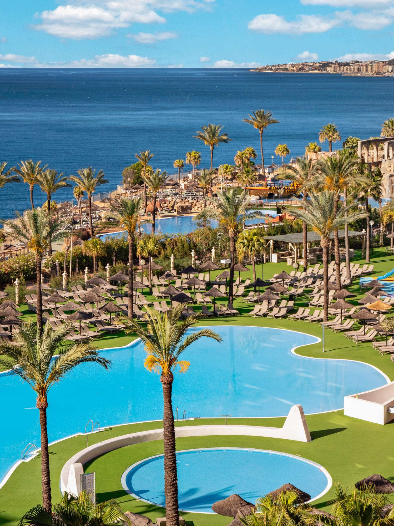 Tropical resort with pools, palm trees, ocean view, and sun loungers.