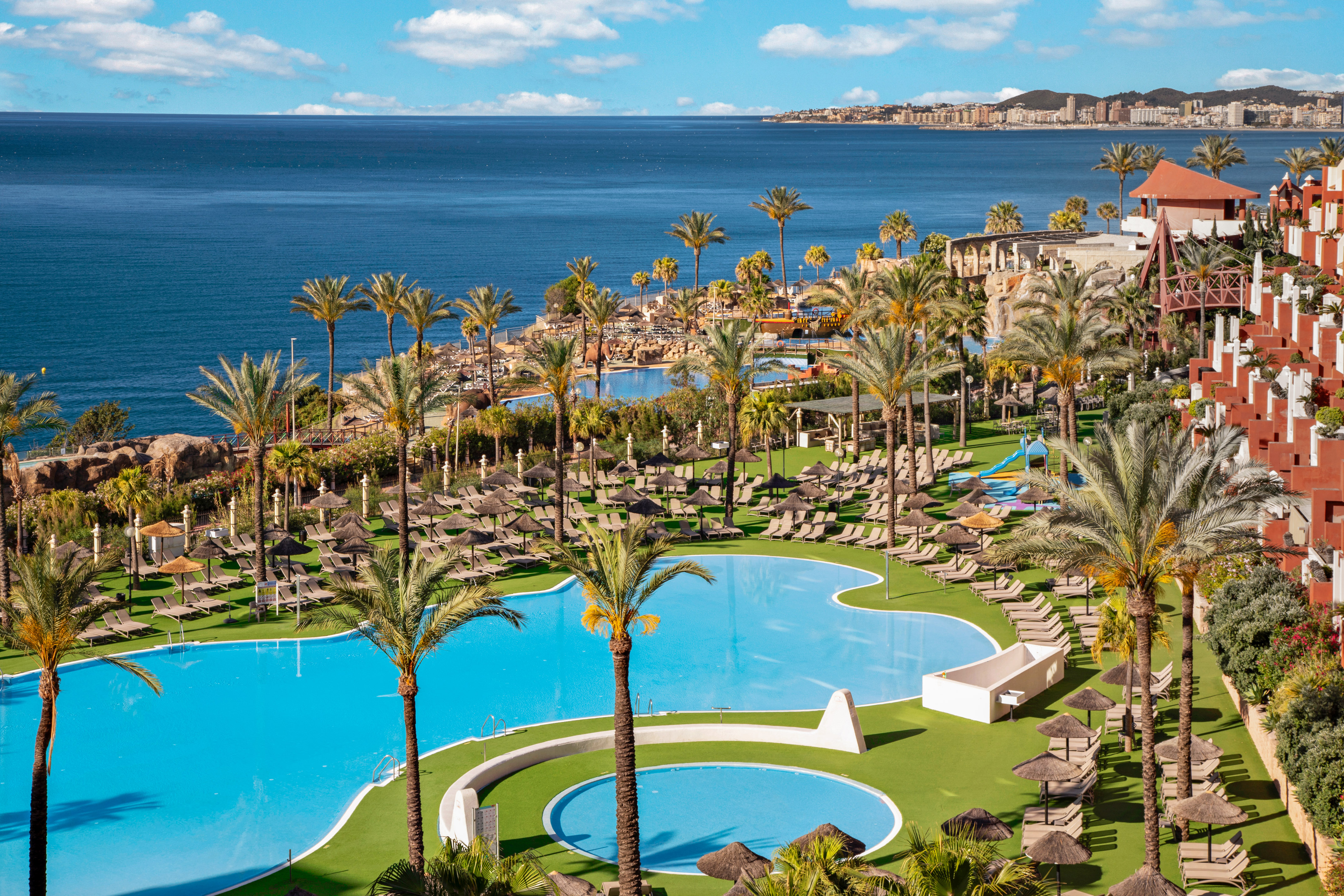 Tropical resort with pools, palm trees, ocean view, and sun loungers.
