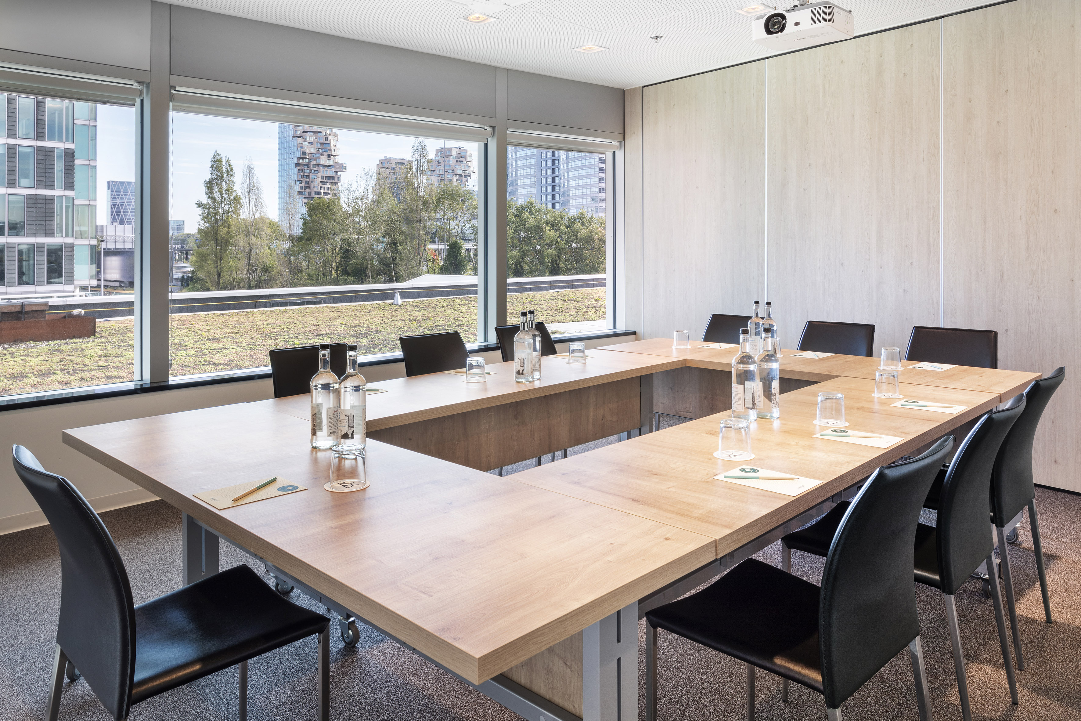 Modern U-shaped meeting room with projector, city view, and green roof.