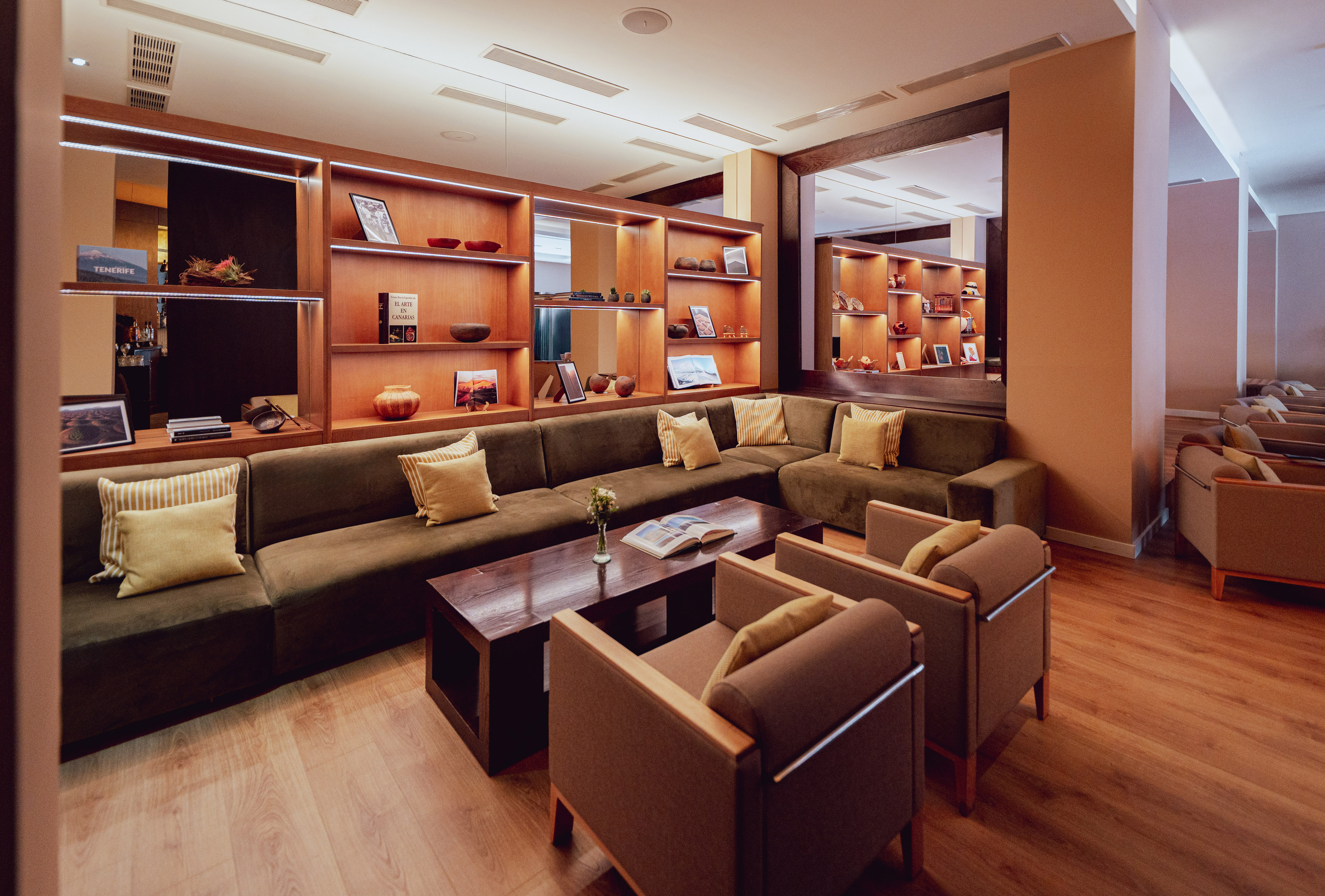 Hotel lounge with green sofa, armchairs, wood table, and illuminated display shelves.