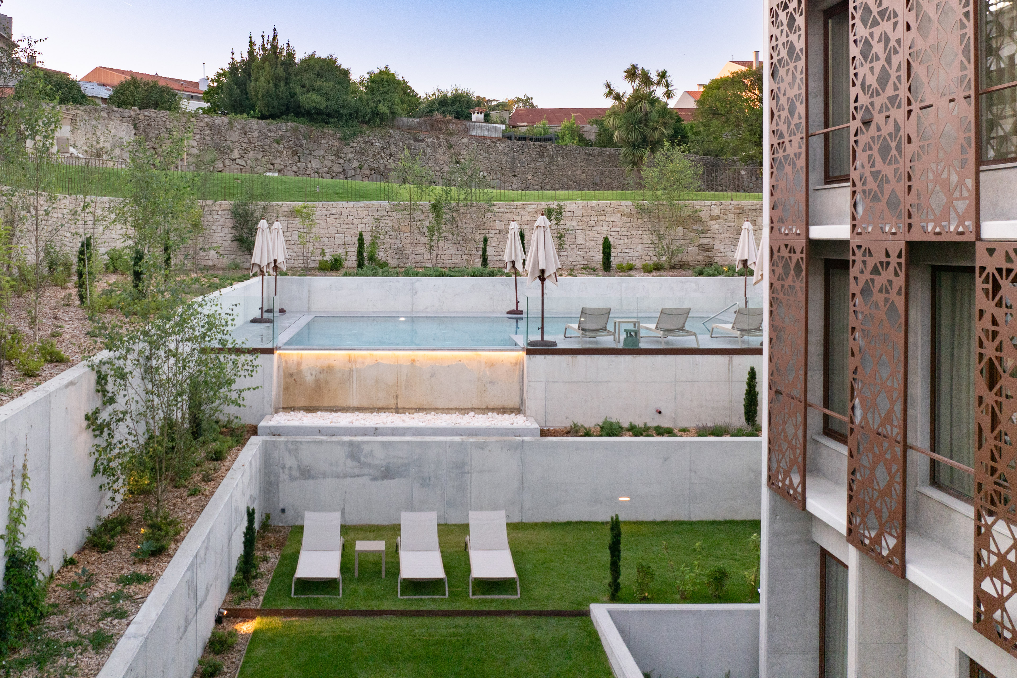 Tiered modern swimming pool and grass terrace with loungers at a resort.