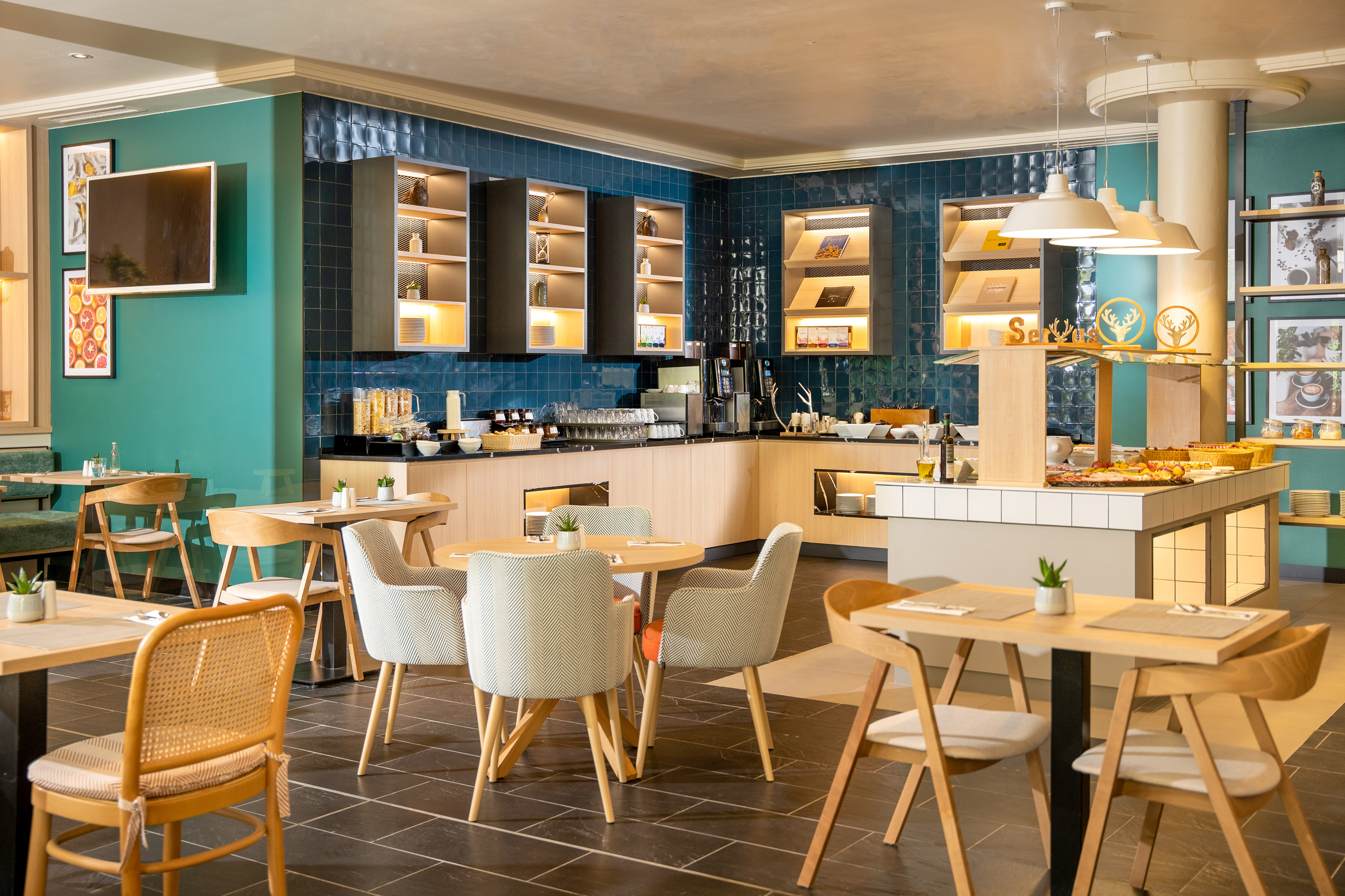 Modern hotel breakfast buffet with stylish dining tables and teal walls.