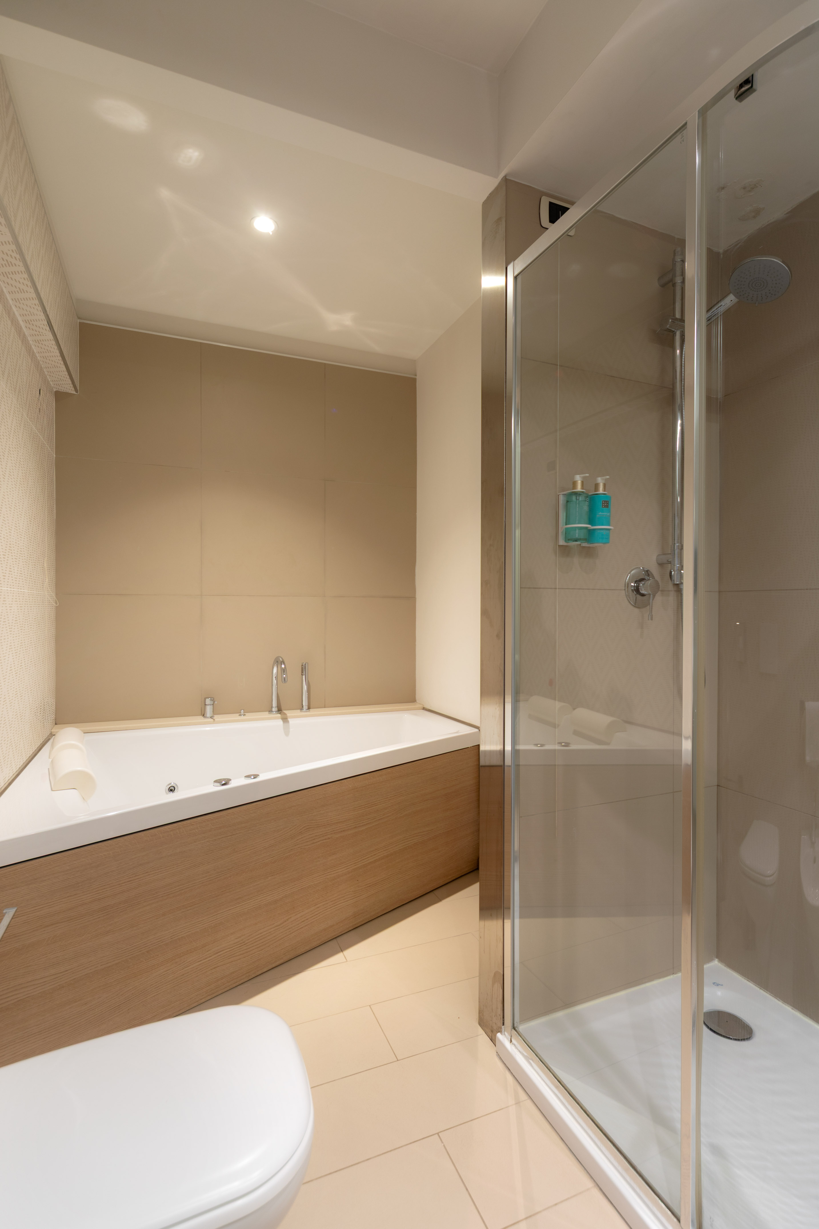 Modern bathroom with corner jacuzzi tub, wood panel, and glass shower.