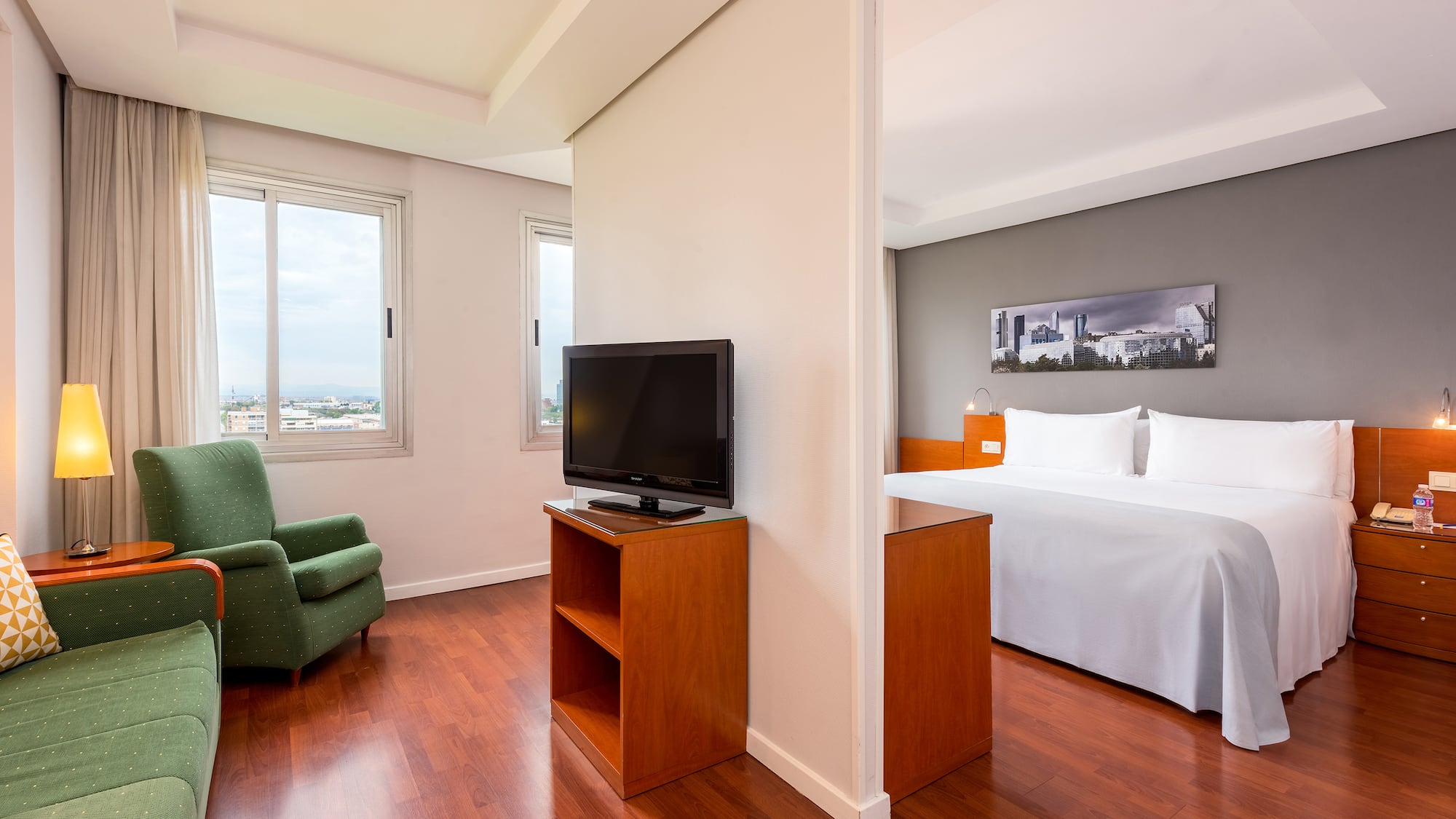 Hotel suite with living room, sofa, TV, king bedroom, and city view.
